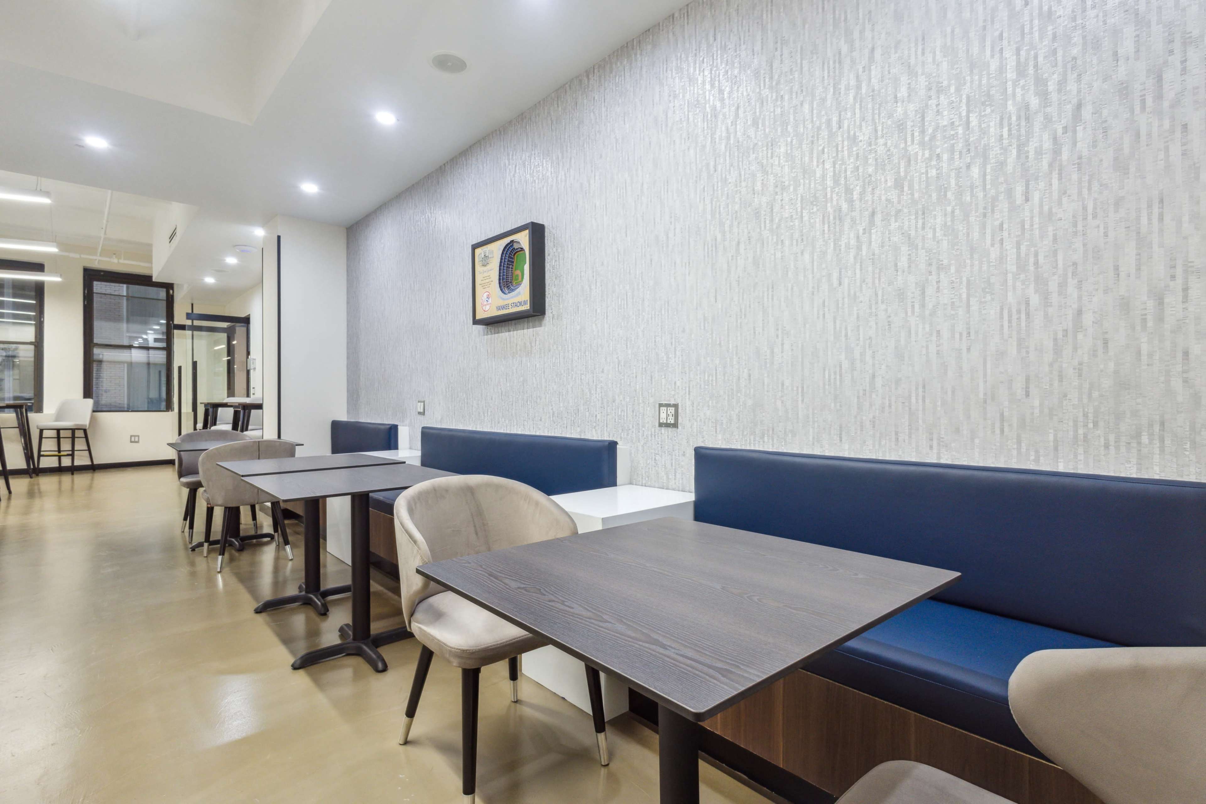 A modern cafe interior with several wooden tables and upholstered chairs arranged against a textured wall.