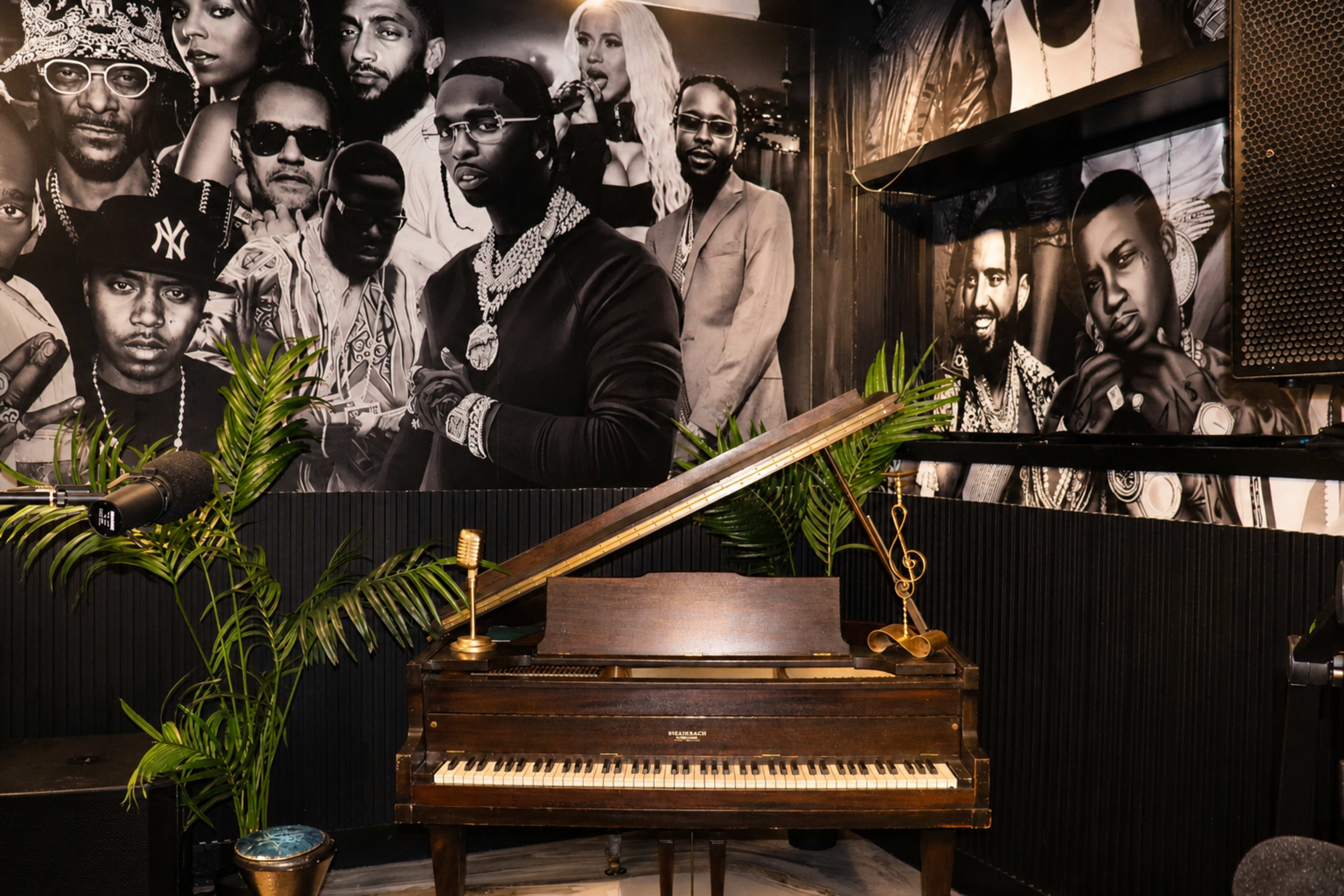 The image features a vintage piano in a room adorned with black-and-white photographs of various artists on the walls.
