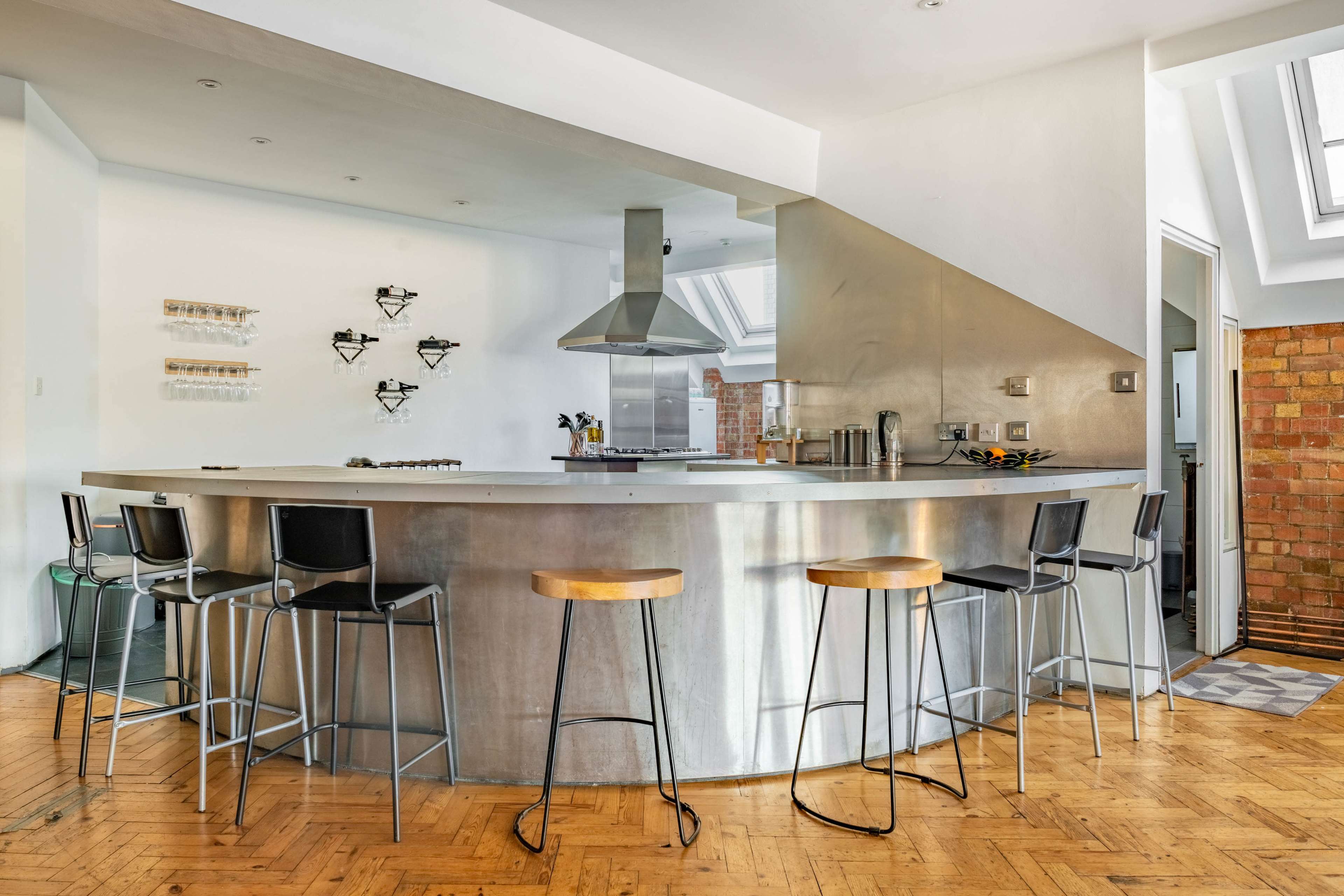 A modern kitchen with a large curved stainless steel counter and black bar stools.