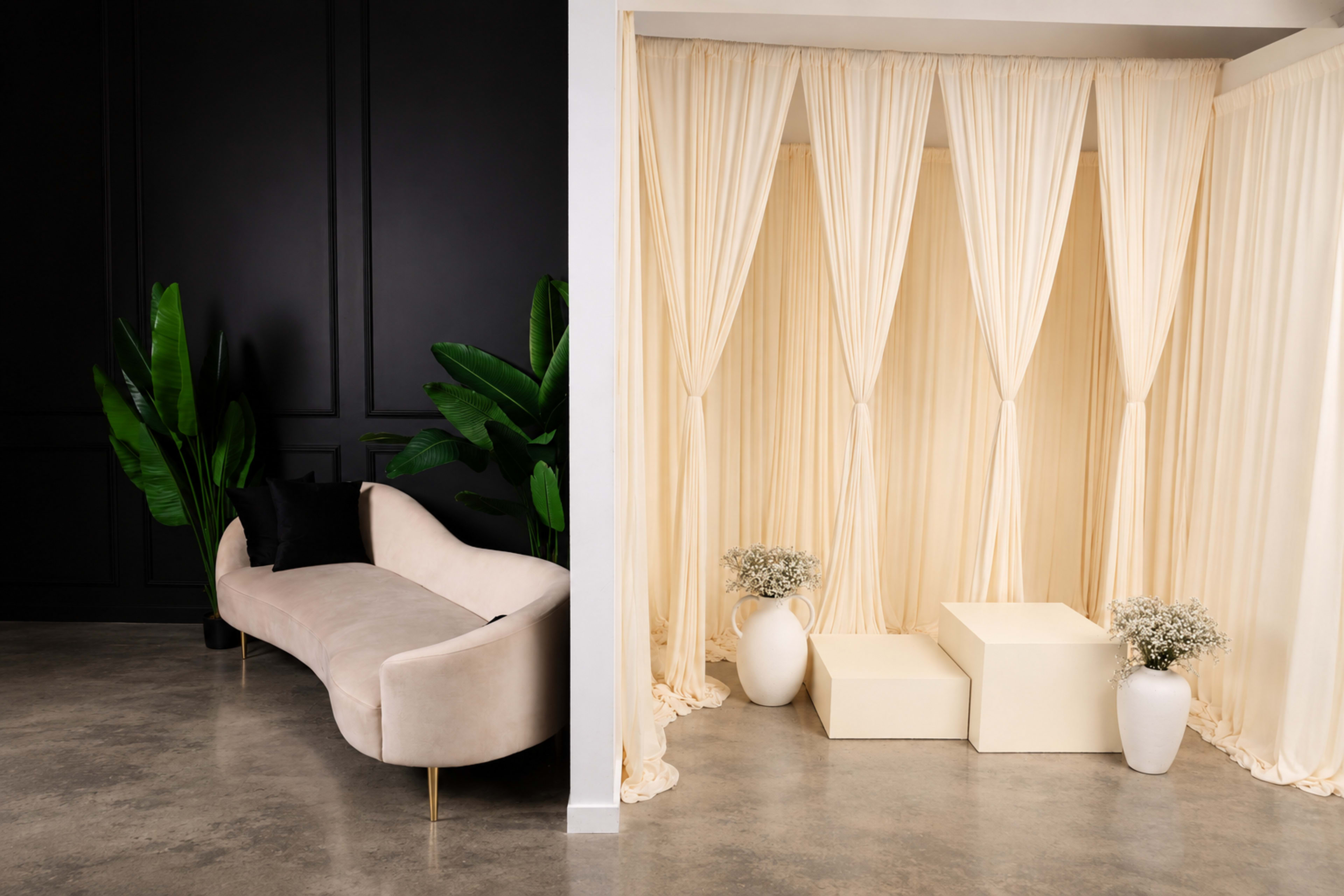 The image shows a modern interior space divided into two sections, one with a light-colored curved sofa and the other featuring cream-colored drapes and minimalistic decor.