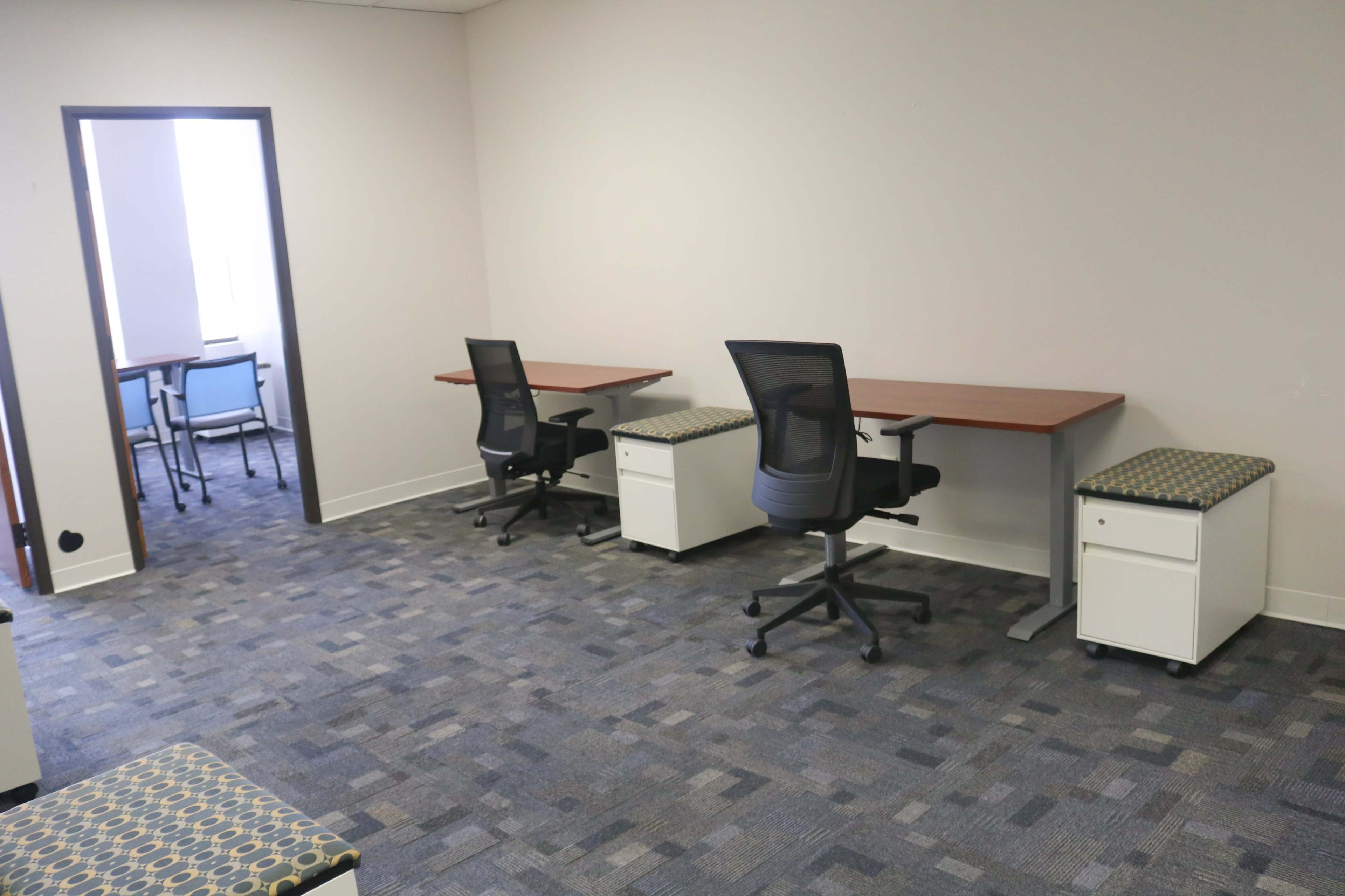 The image shows a clean office space with several desks and chairs arranged neatly, along with storage units beneath the desks.