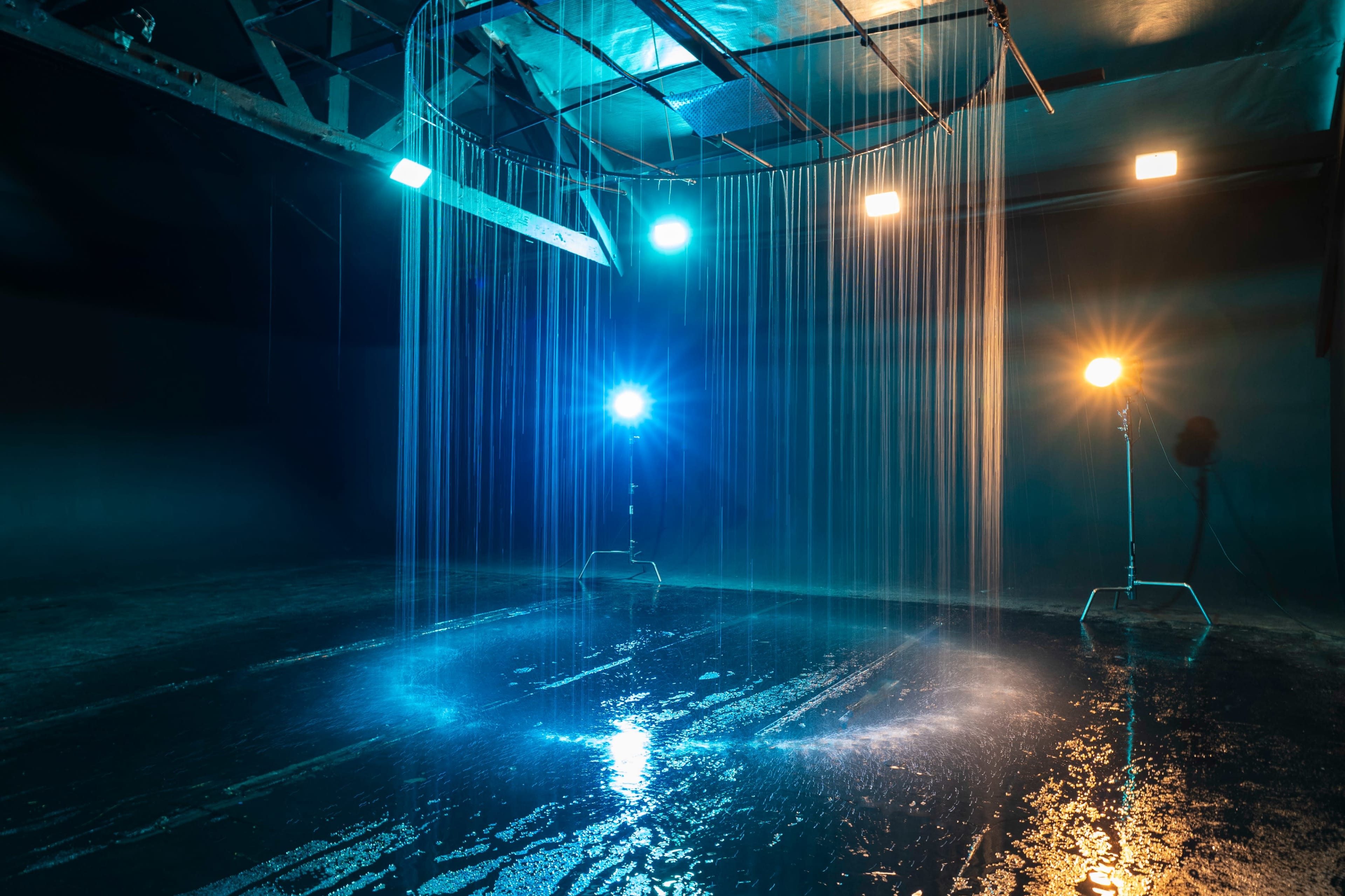 A dark studio space with overhead lights illuminating vertical streams of water falling onto a reflective surface.