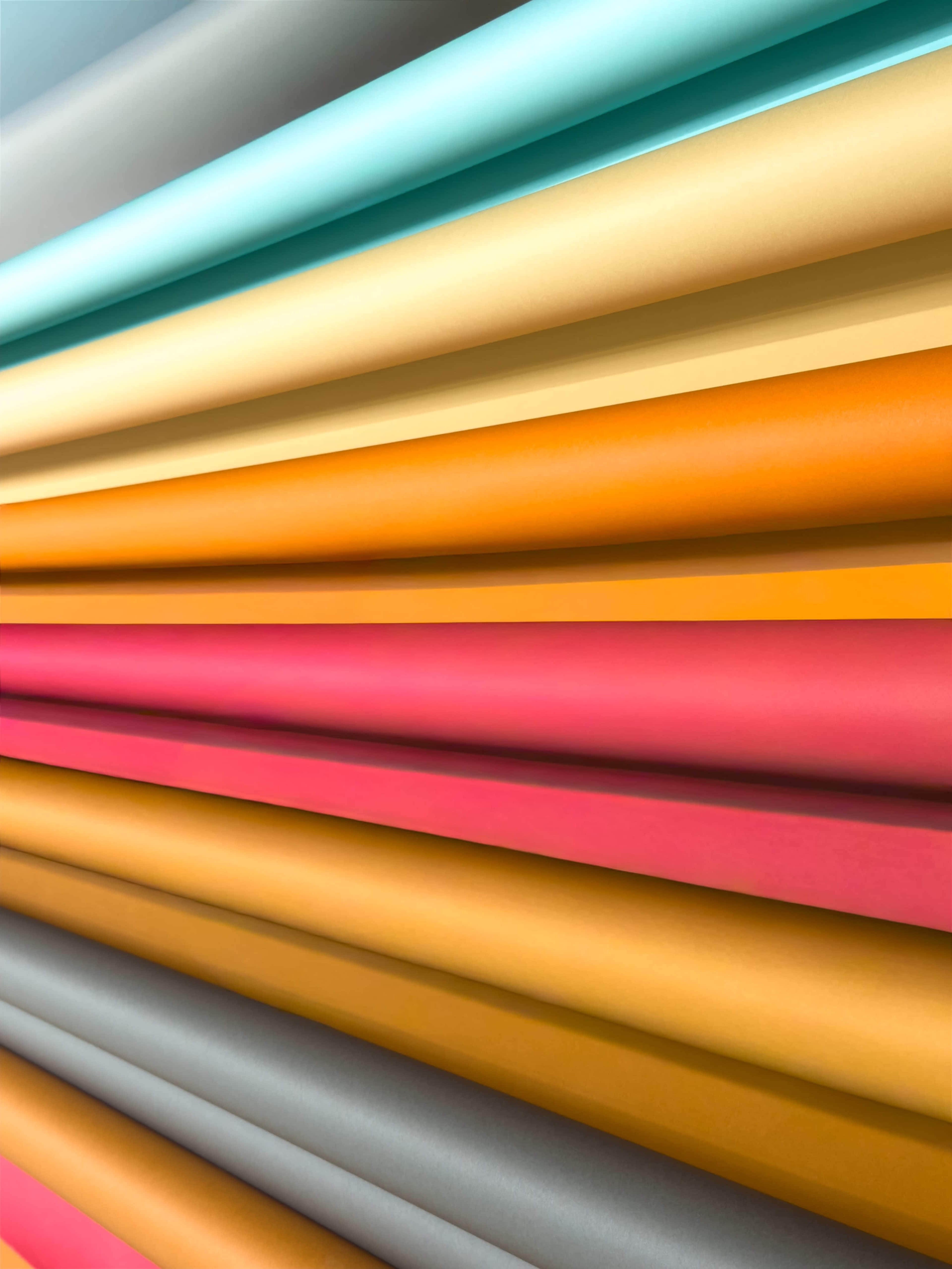 The image shows a stack of colorful sheets of paper arranged in horizontal layers, displaying various hues like teal, yellow, orange, pink, and gray.