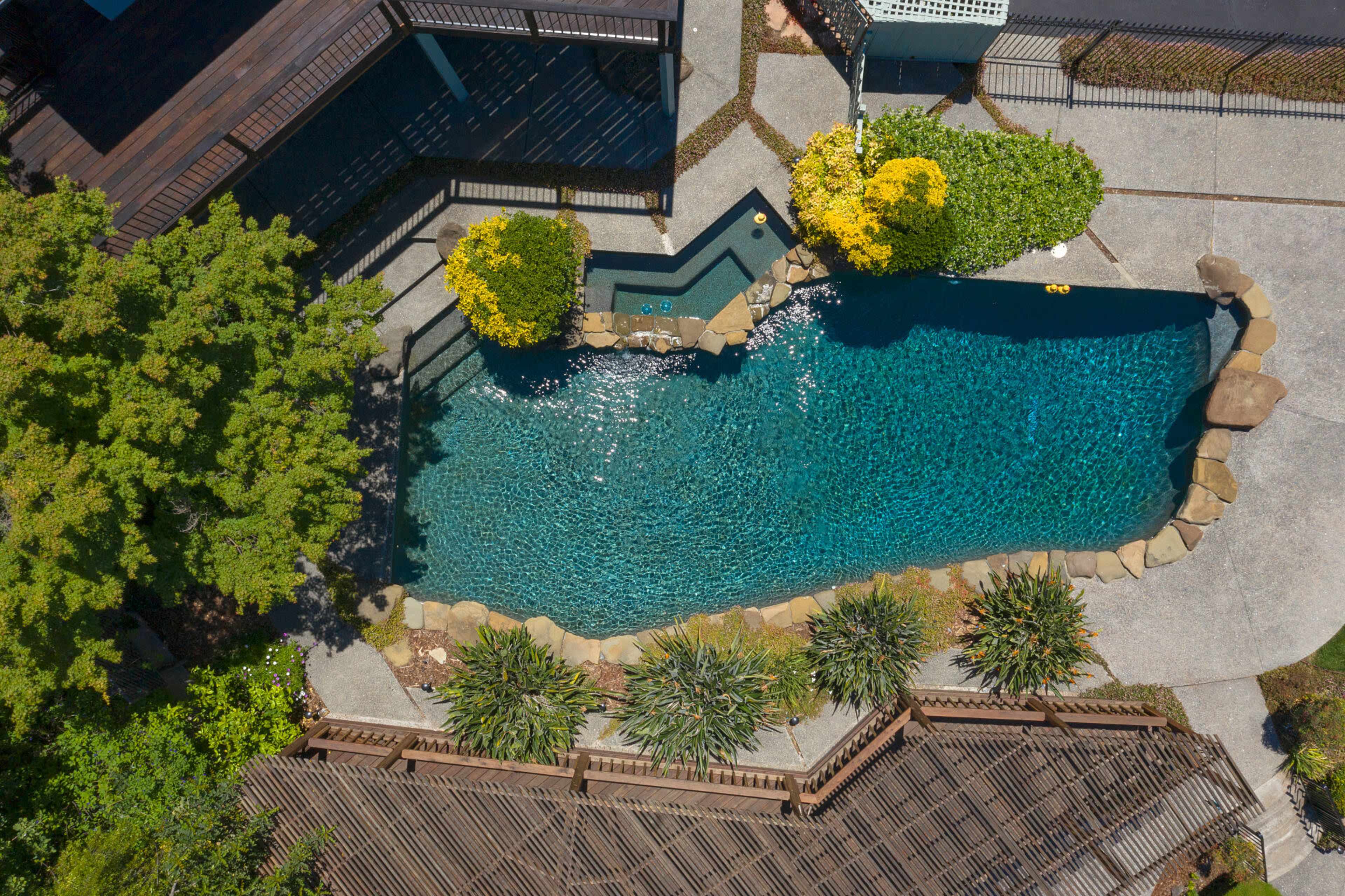 An aerial view showcases a landscaped backyard featuring a swimming pool surrounded by stone edging and greenery.