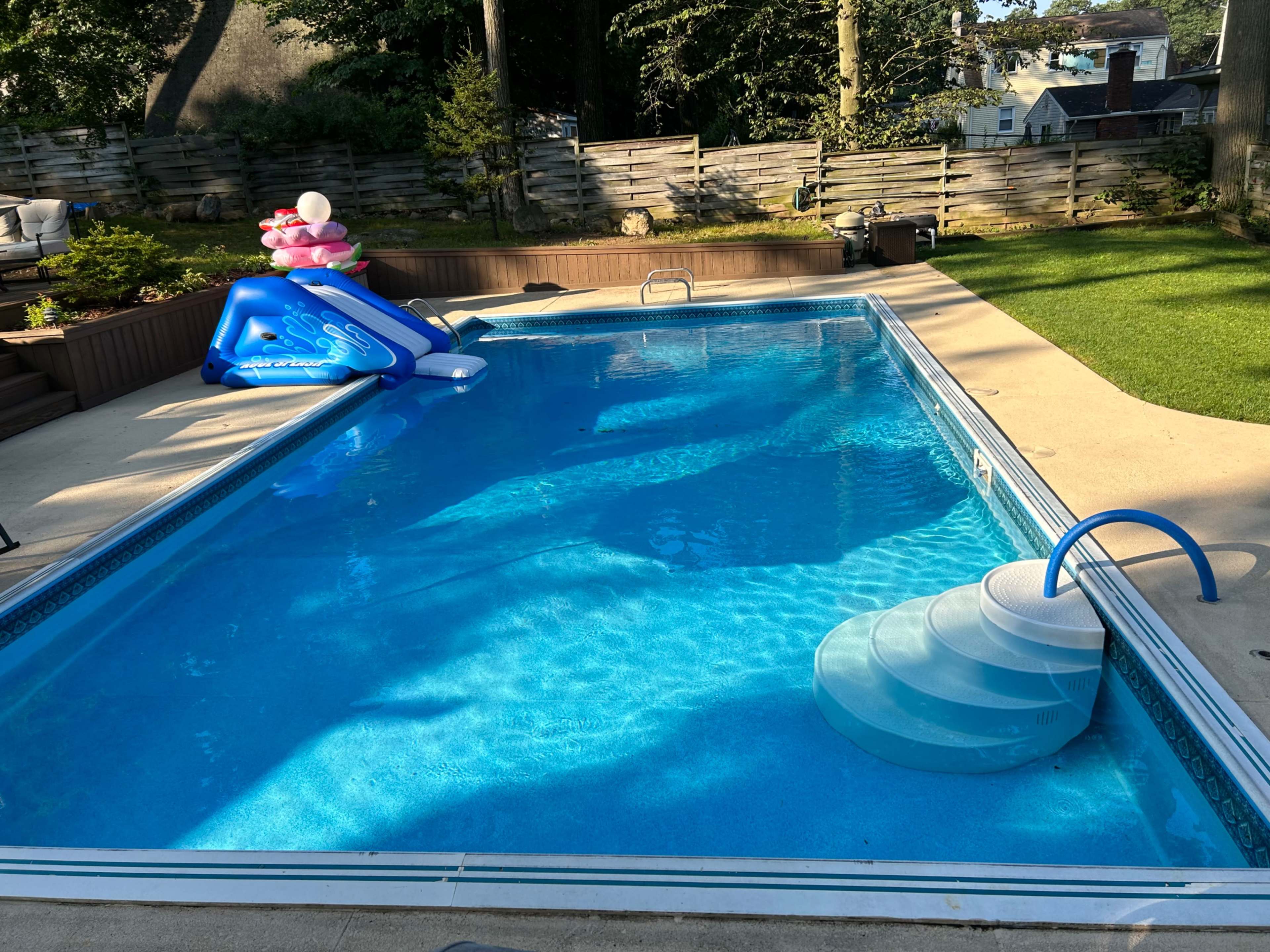 A clean swimming pool is surrounded by a patio area, featuring blue water slides and a slide entry.