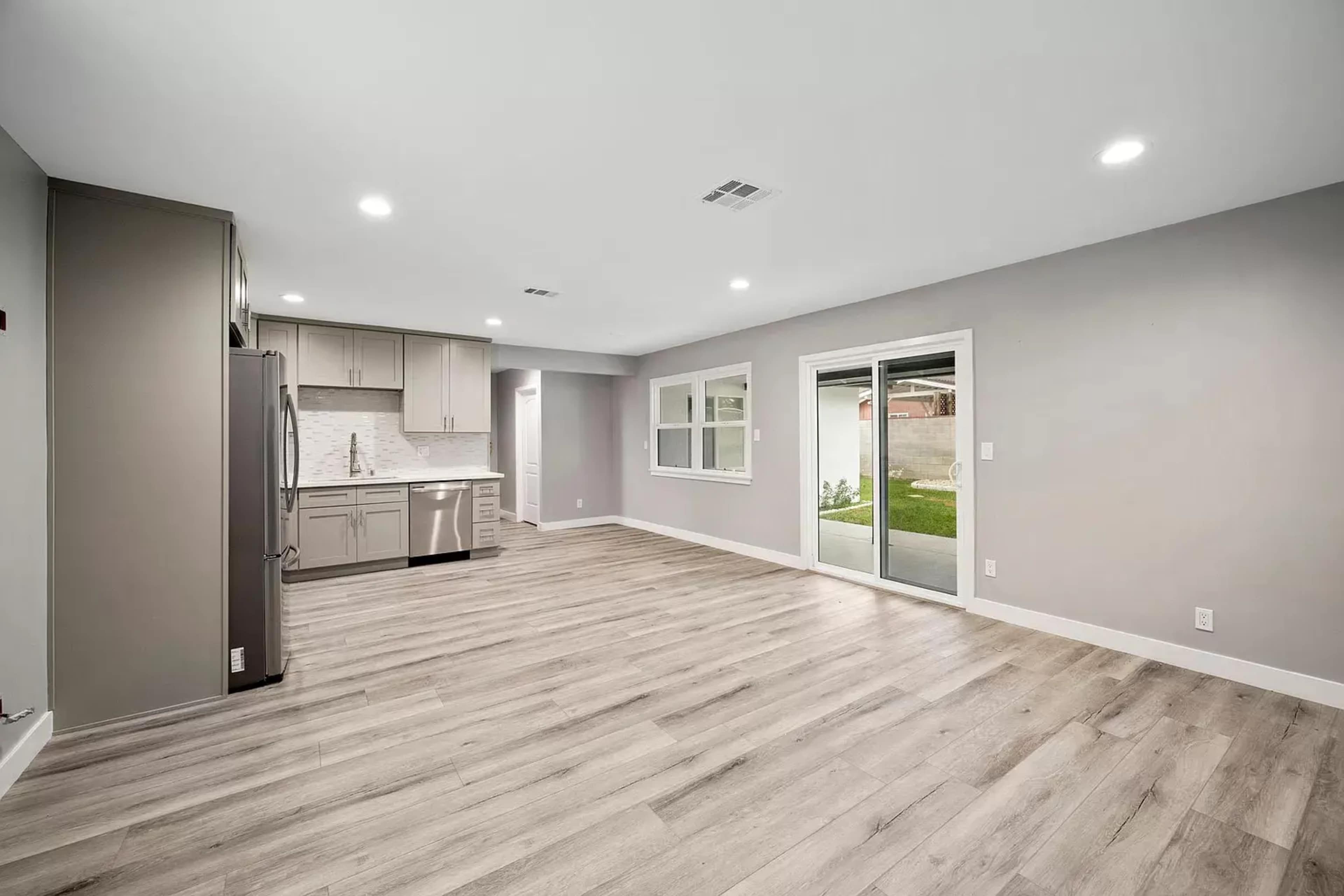 A modern kitchen and living area with light wood flooring and sliding glass doors leading to an outdoor space.