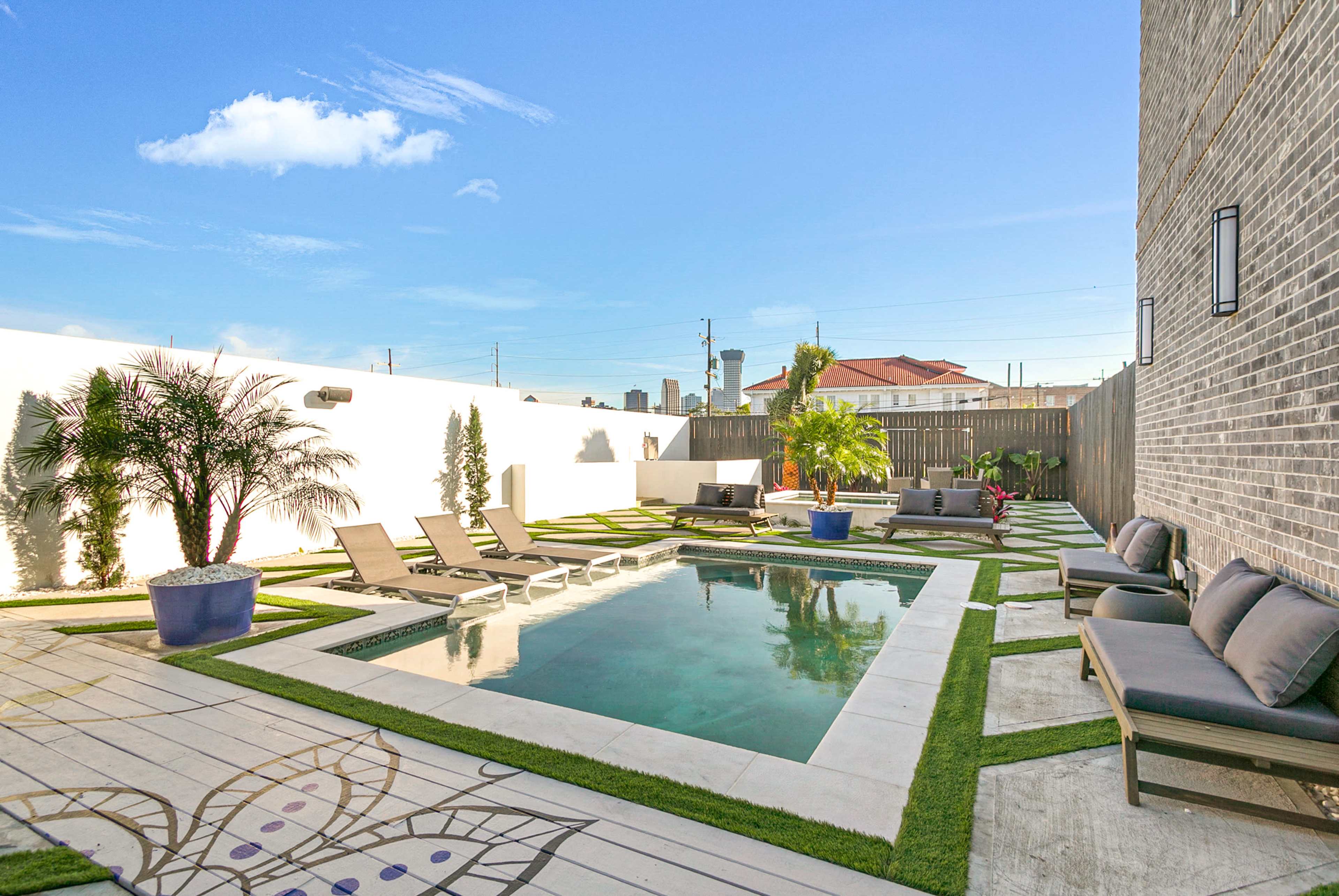 A modern backyard featuring a rectangular swimming pool surrounded by lounge chairs, decorative plants, and stone pathways.