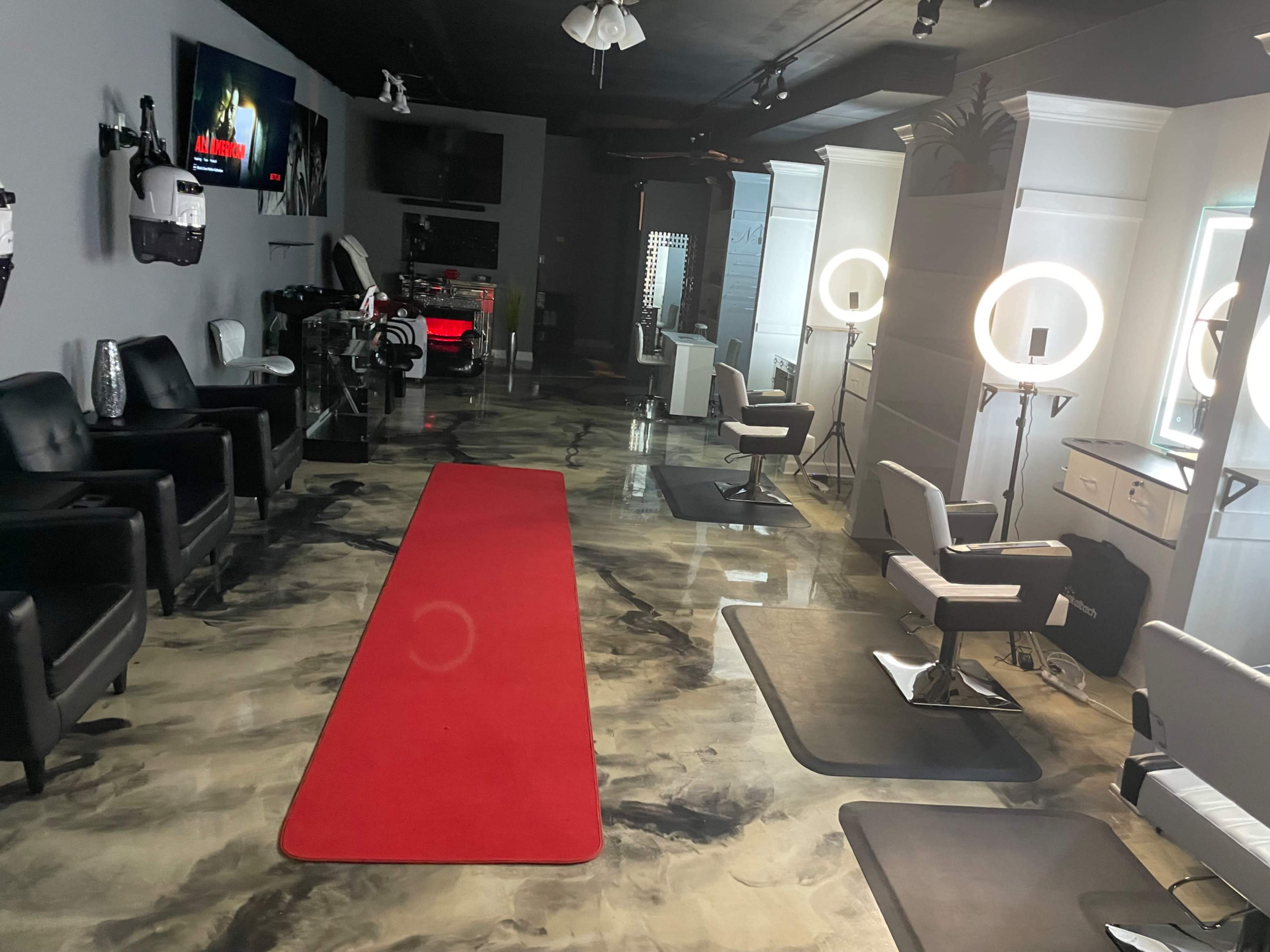 A modern salon interior with black leather chairs, styling stations, a red carpet, and ring lights, illuminated by soft overhead lighting.