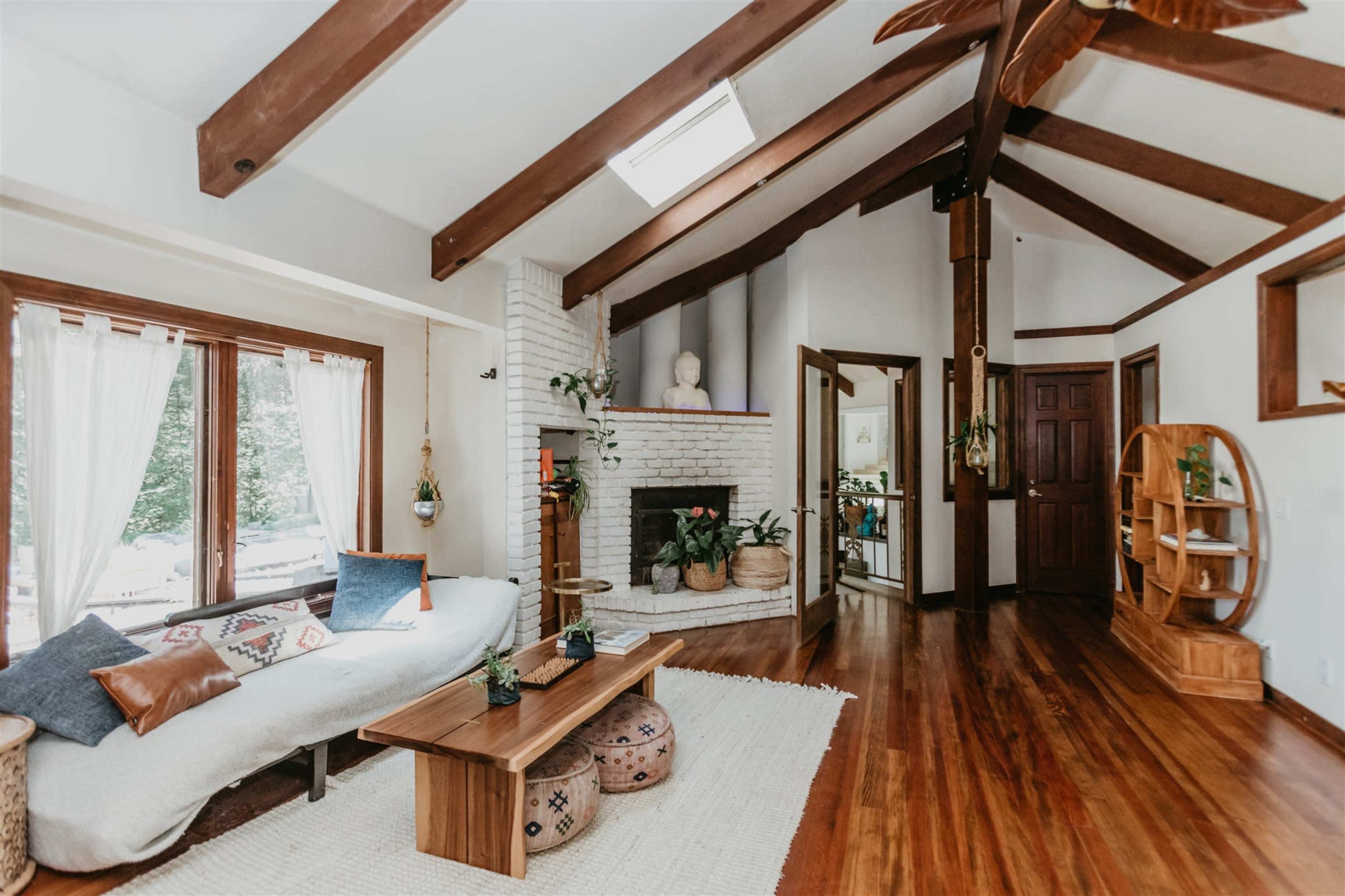 The living room features a white sofa, wooden beams on the ceiling, and a fireplace adorned with decorative items.