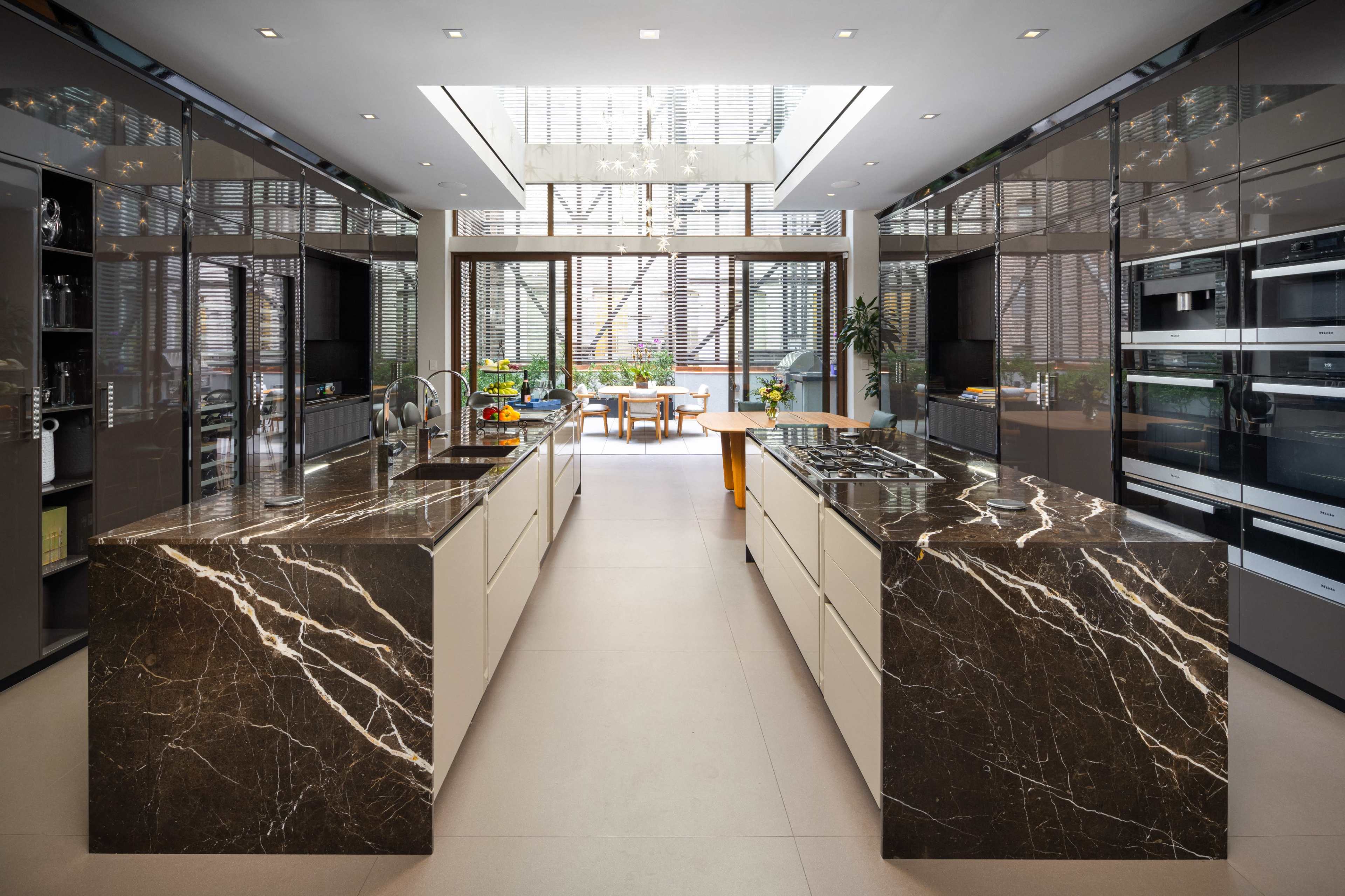 The image shows a modern kitchen featuring dark marble countertops, sleek cabinetry, and large windows that allow natural light to fill the space.
