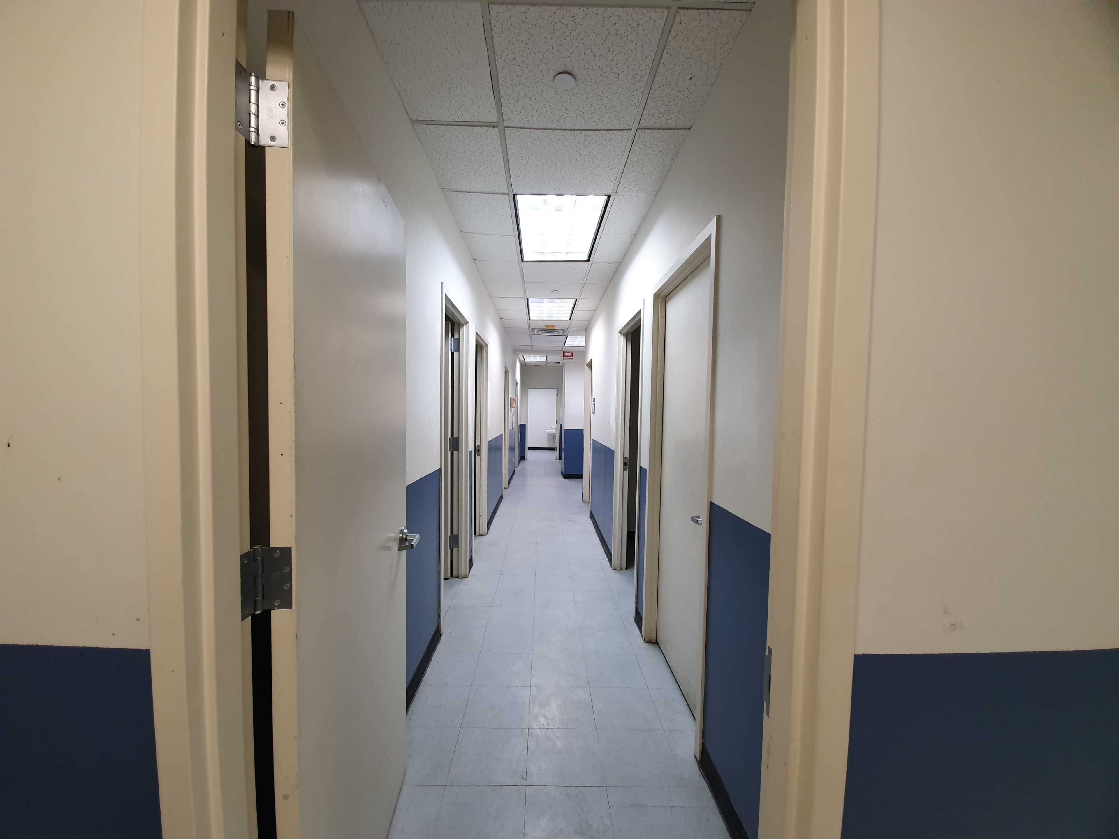 A hallway with doors on both sides and blue-painted lower walls leads to an illuminated area at the far end.