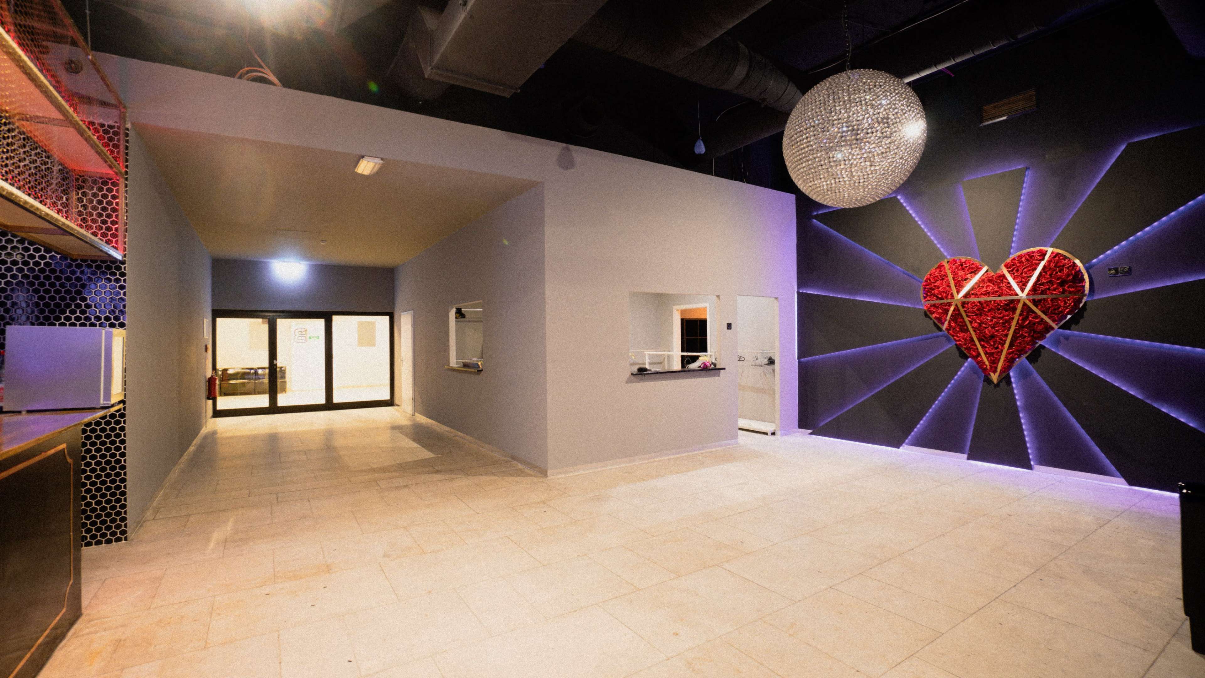 A spacious interior with a heart-shaped artwork on the wall, illuminated by a large disco ball hanging from the ceiling.