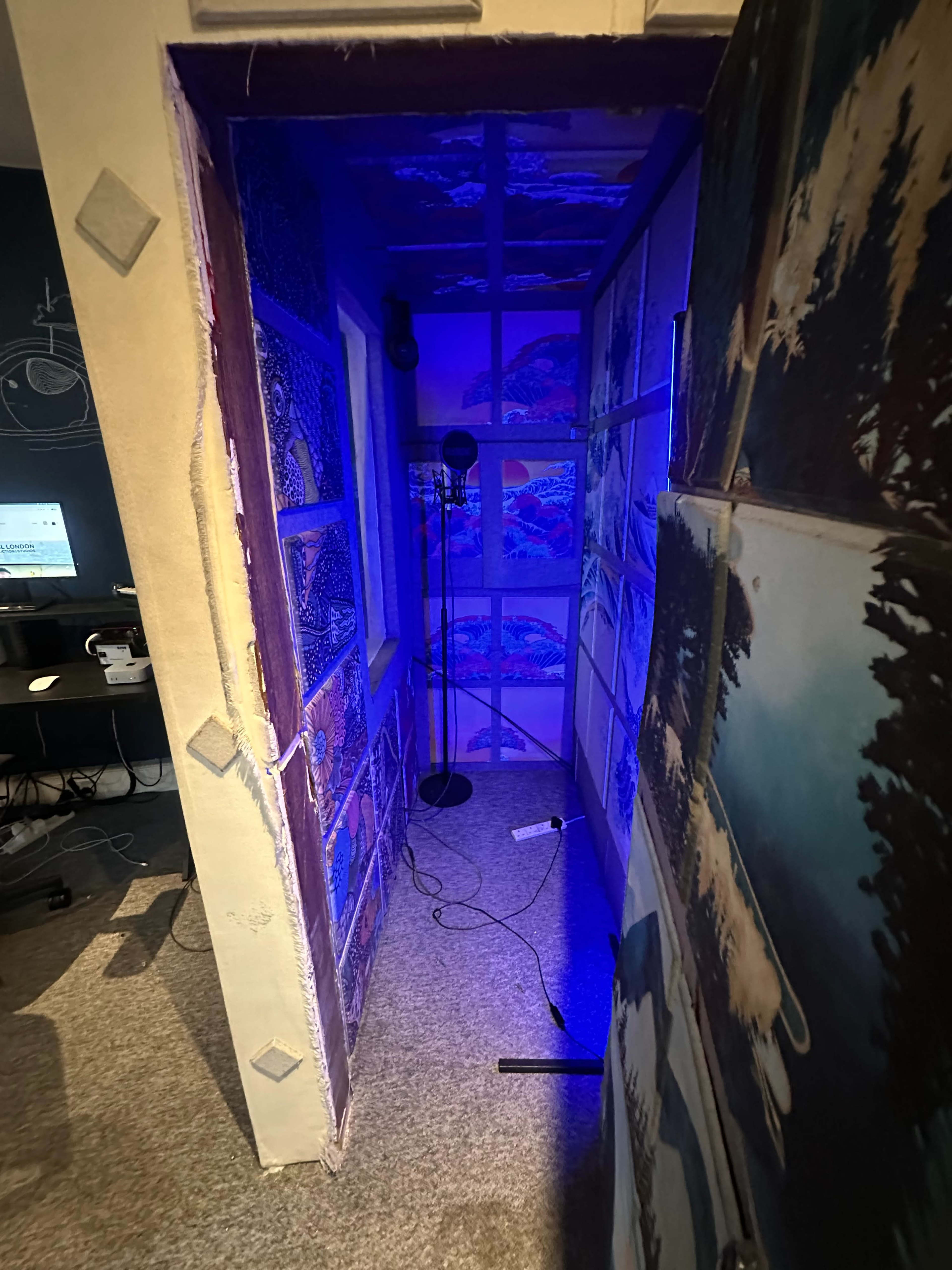 The image shows a narrow hallway with colorful wall art and a microphone stand under blue lighting.