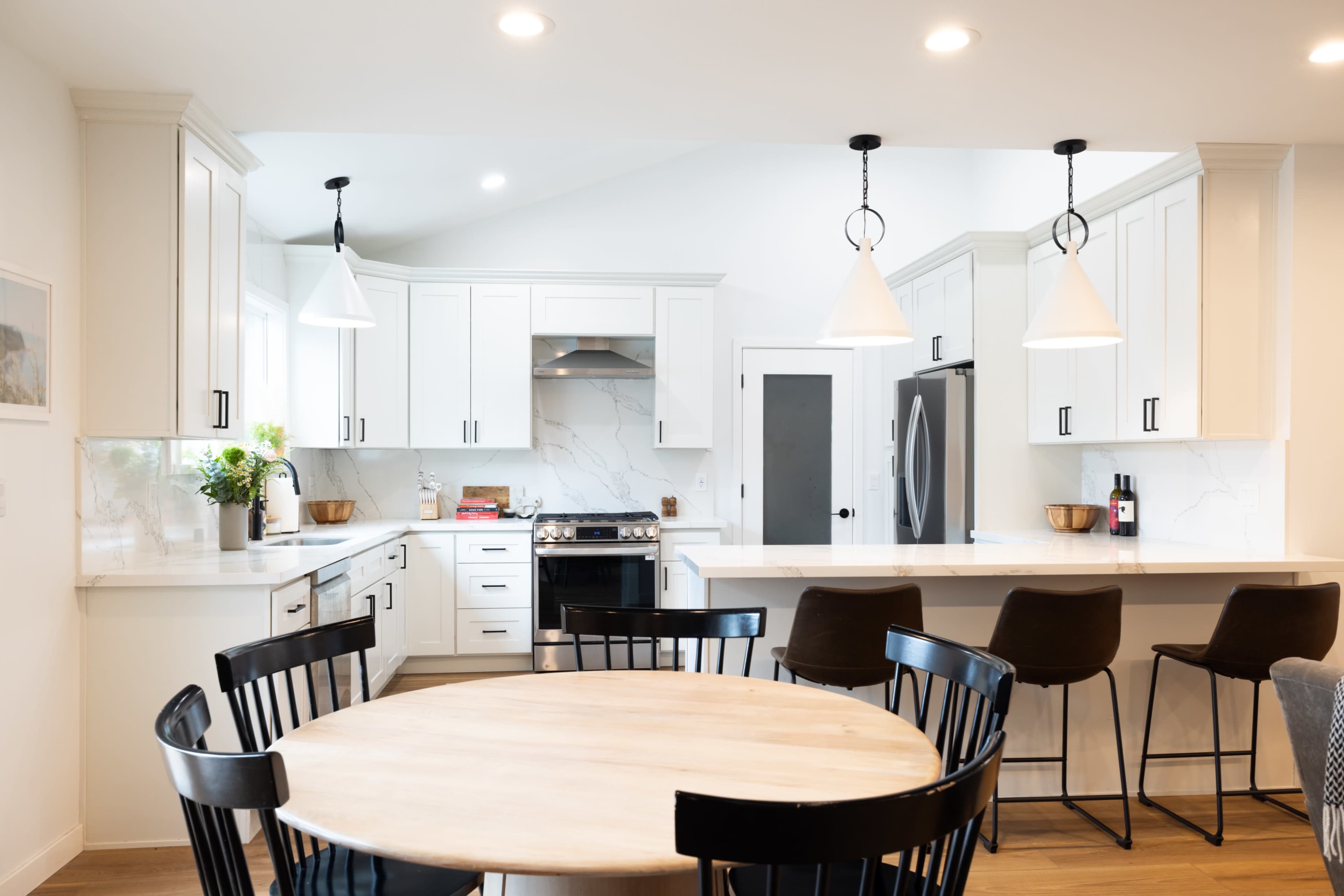 A modern kitchen features white cabinetry, a large island with bar seating, and pendant lighting above a circular dining table.