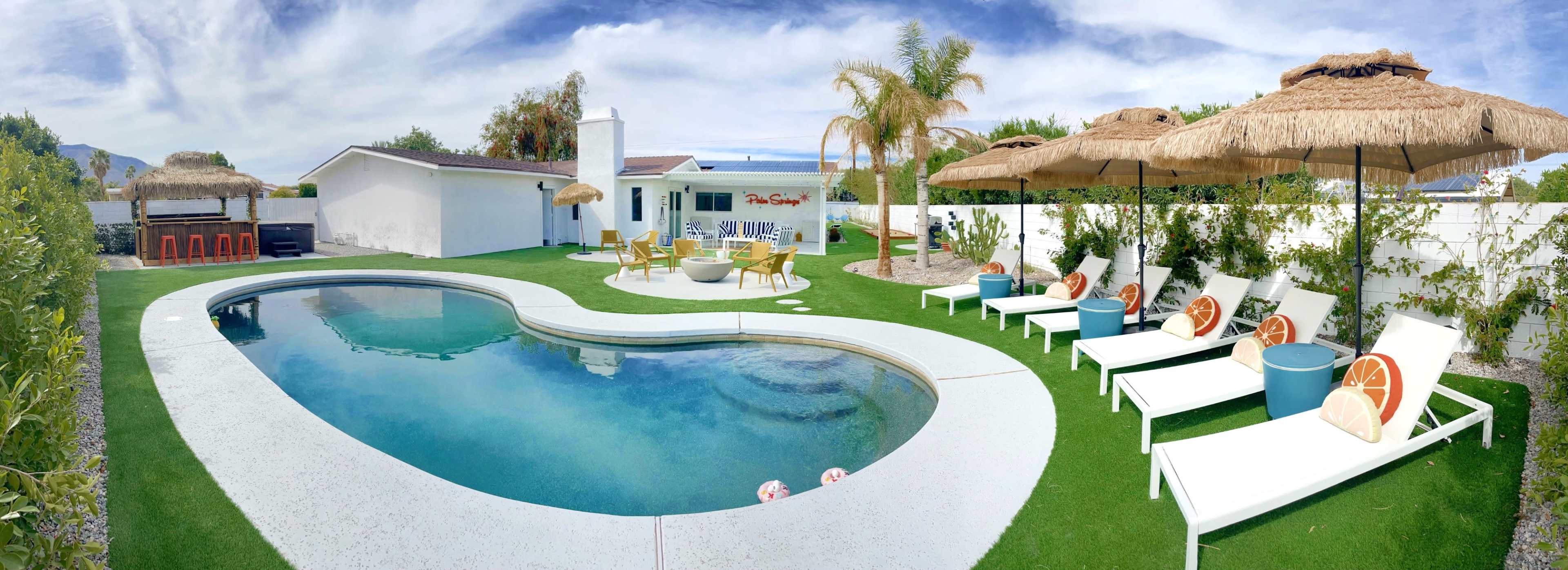 The image shows a landscaped backyard featuring a swimming pool, lounge chairs, and thatched umbrellas surrounding a well-maintained grassy area.