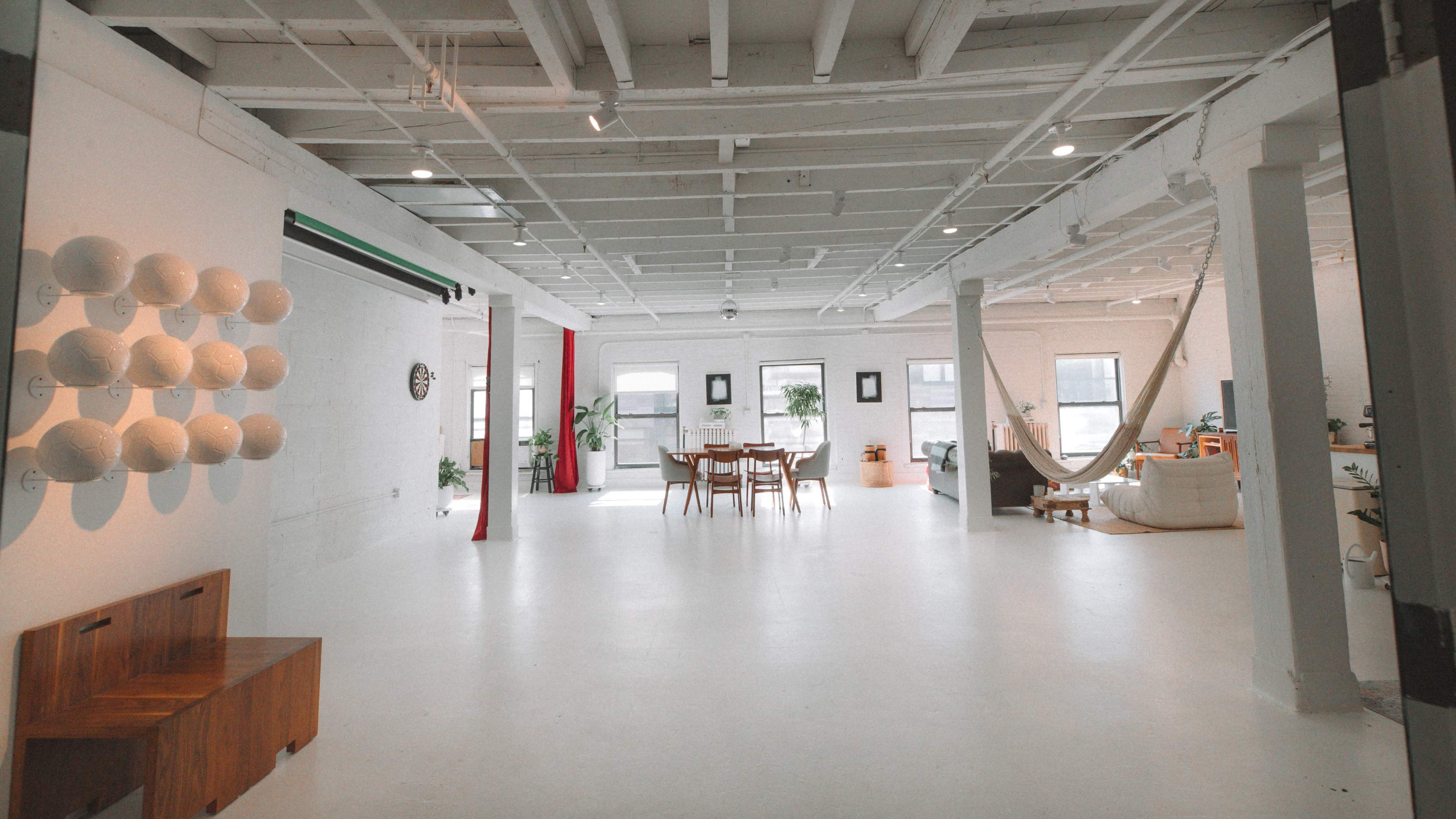 The image shows a spacious, bright interior with a dining area, a hammock, and various plants arranged throughout.