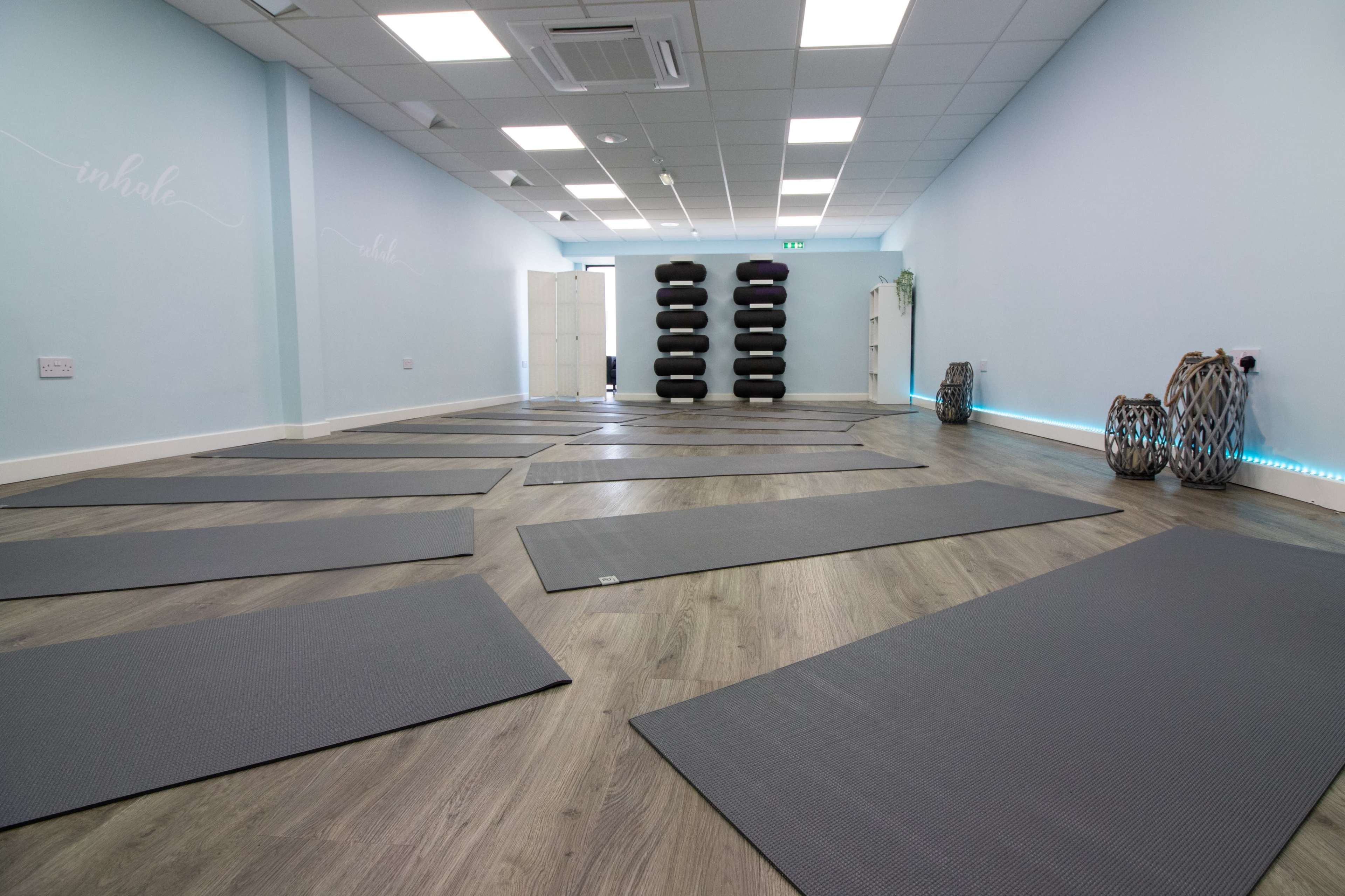 A yoga studio with several gray mats arranged on a wooden floor, against a light blue wall.