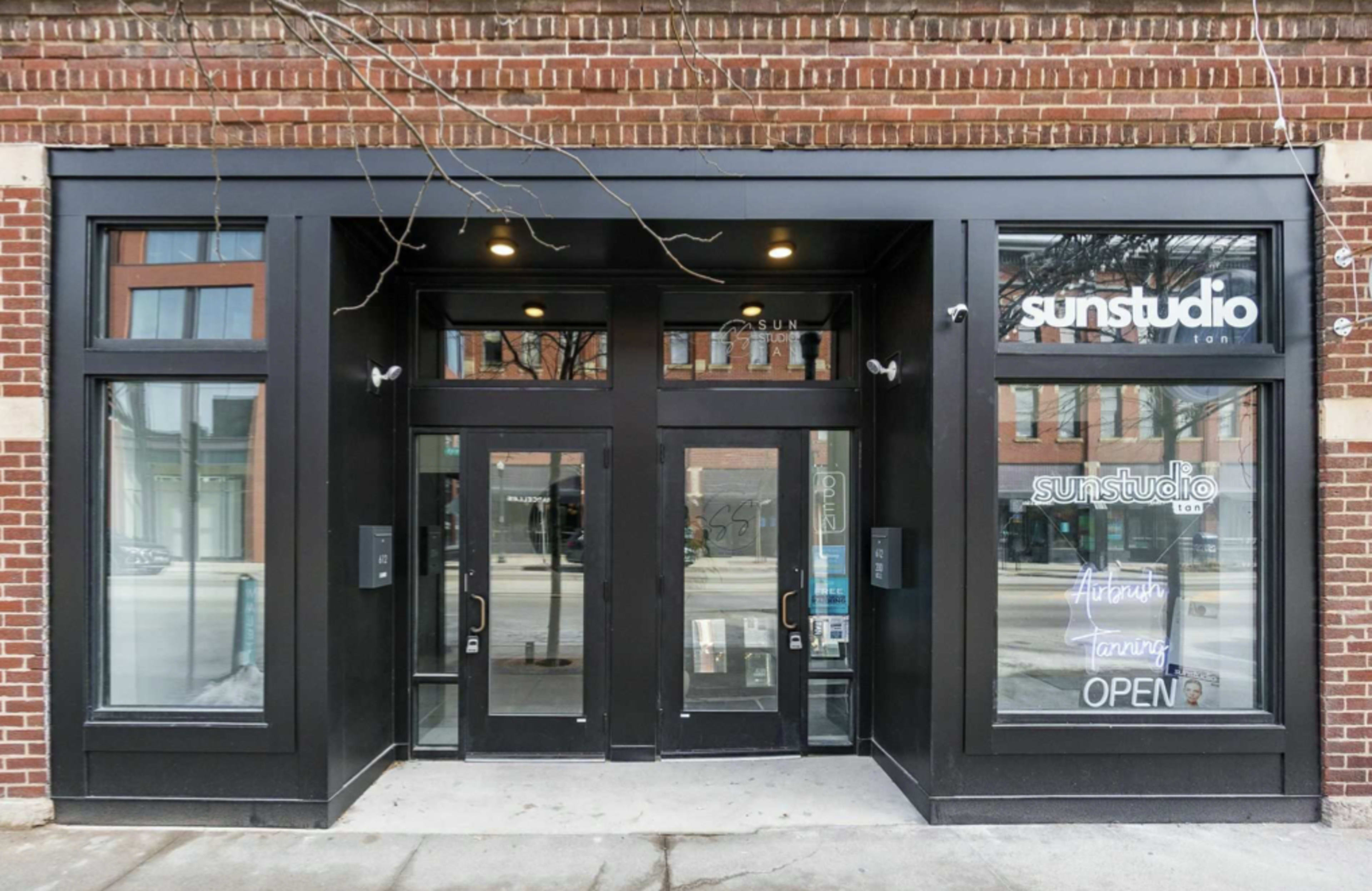 The entrance of a brick building features large glass doors and a sign indicating that Sun Studio is open, with additional signage about fitness training.