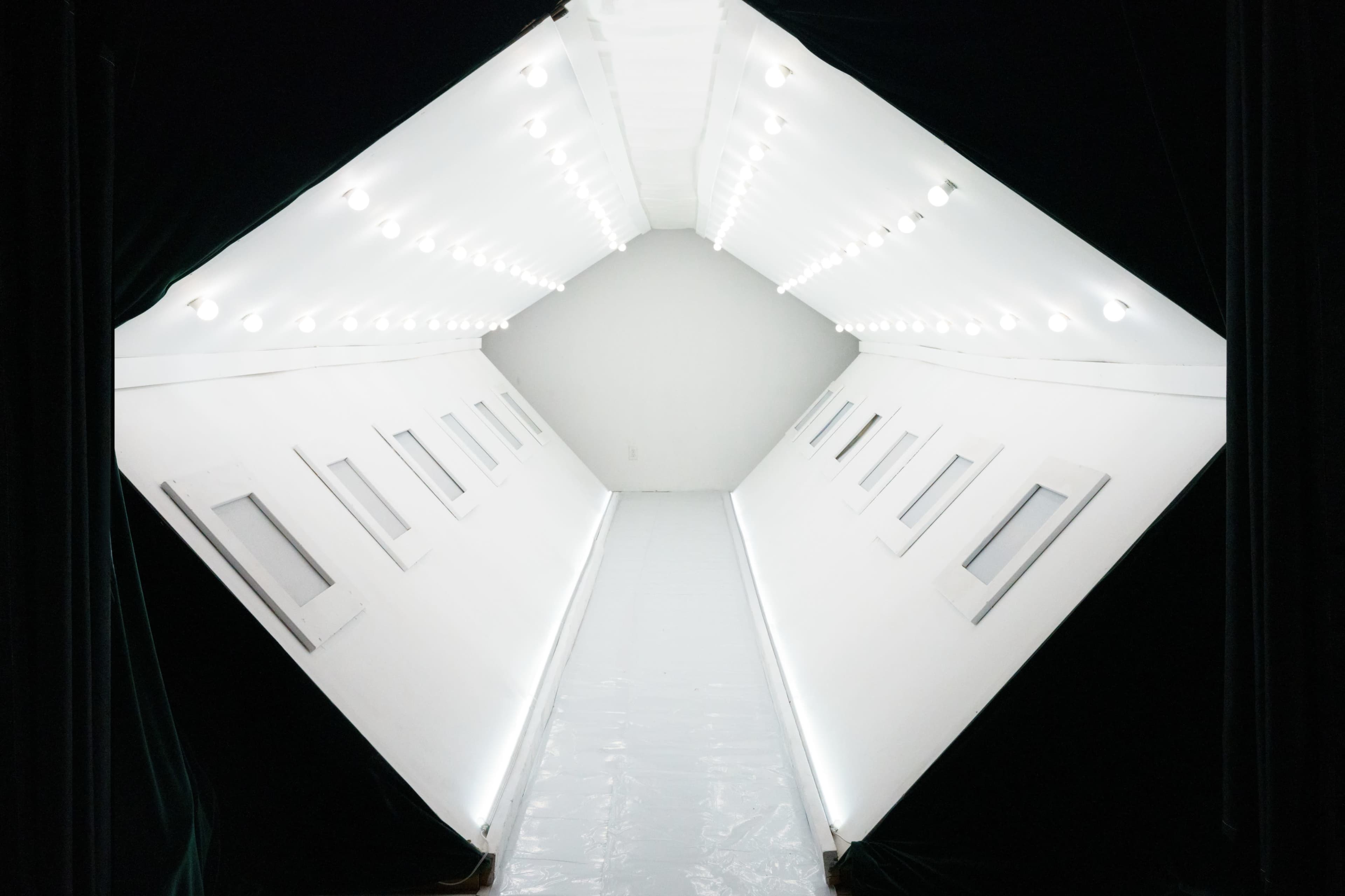 The image shows a bright, symmetrical corridor with a series of lights along the ceiling and windows along the walls.