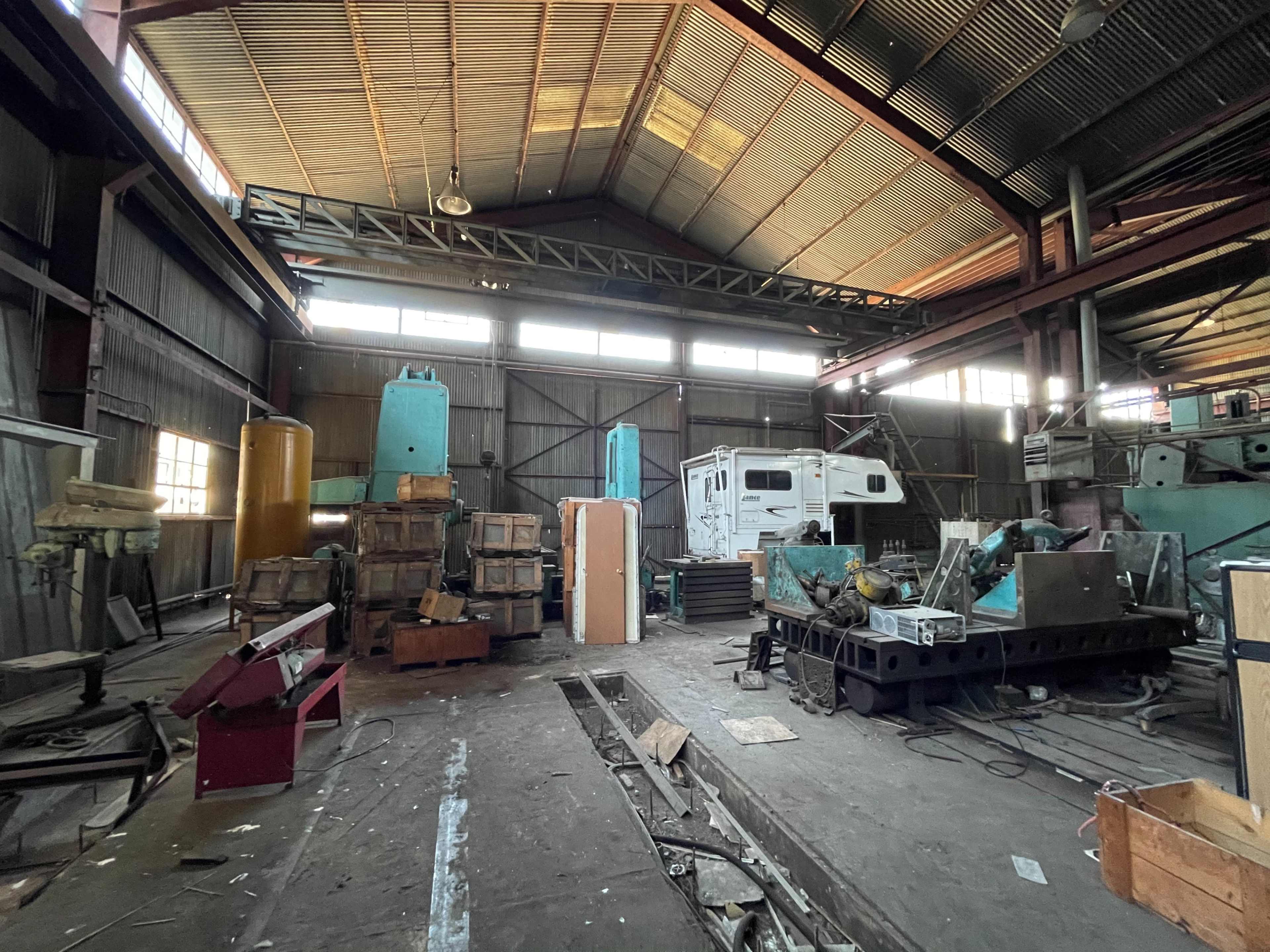 The image shows an industrial warehouse filled with machinery, stacked crates, and equipment scattered across the concrete floor.