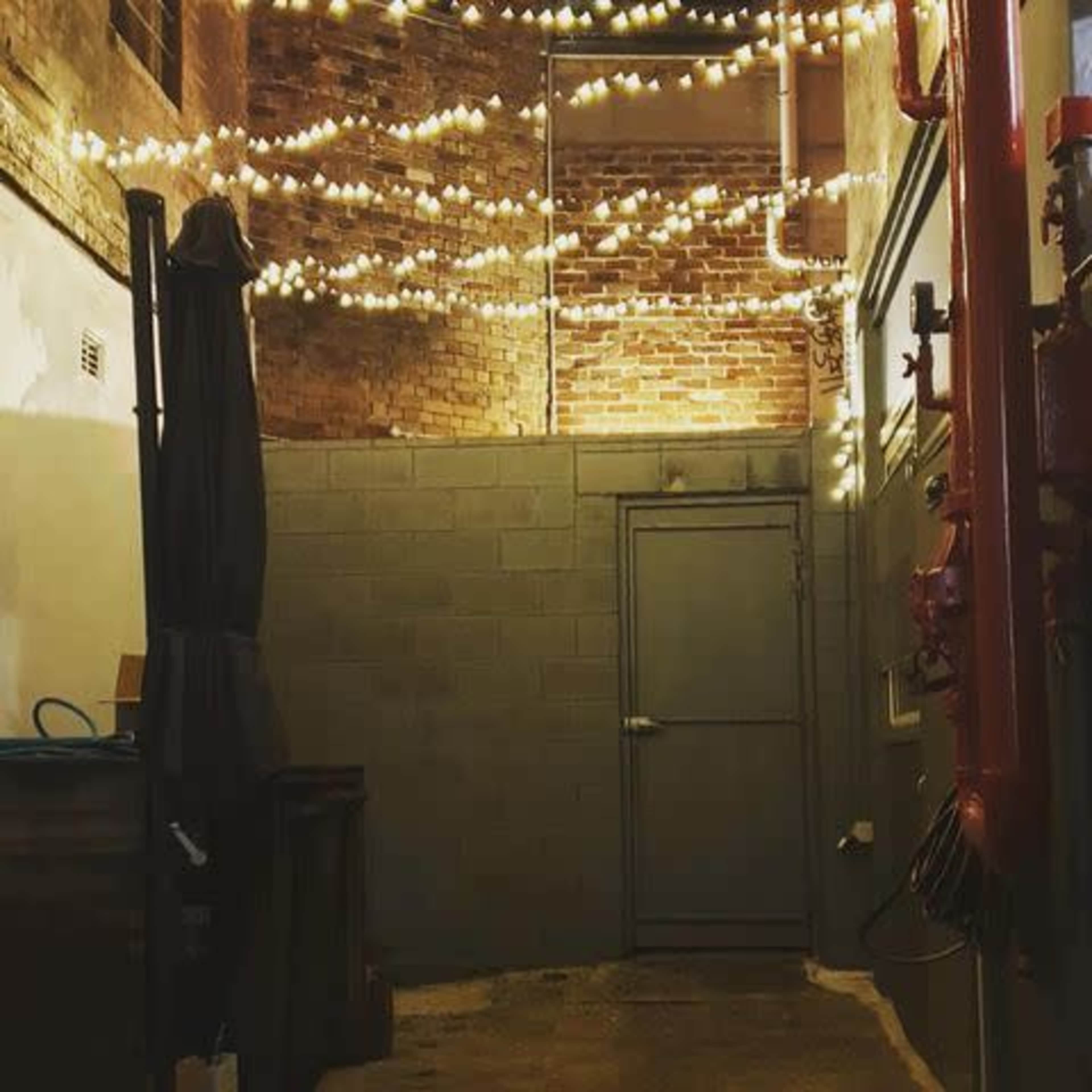 The scene features a narrow alleyway with brick walls, string lights overhead, and a closed metal door at the end.