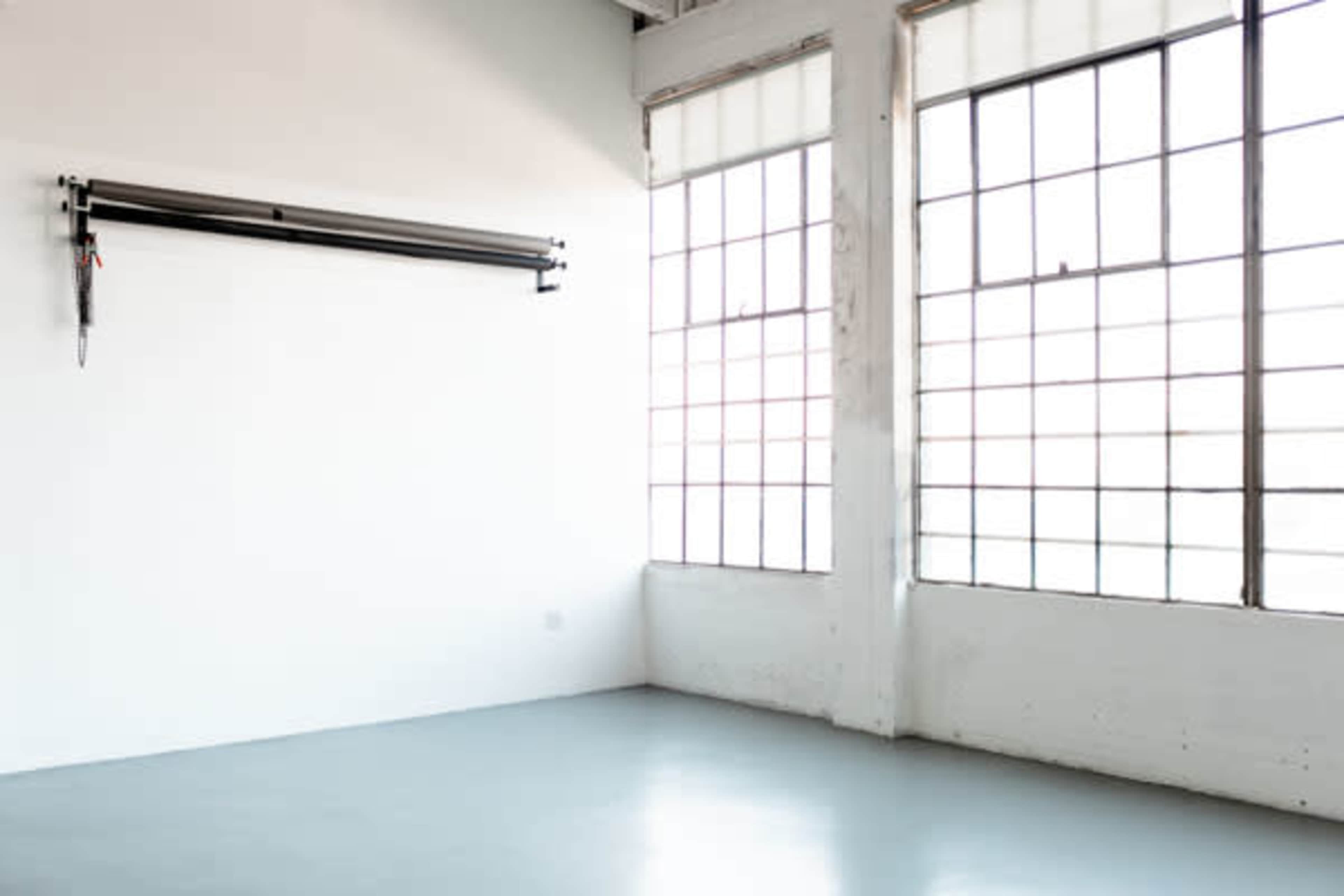 A sparsely furnished room with two large windows and a black roller system mounted on a white wall.