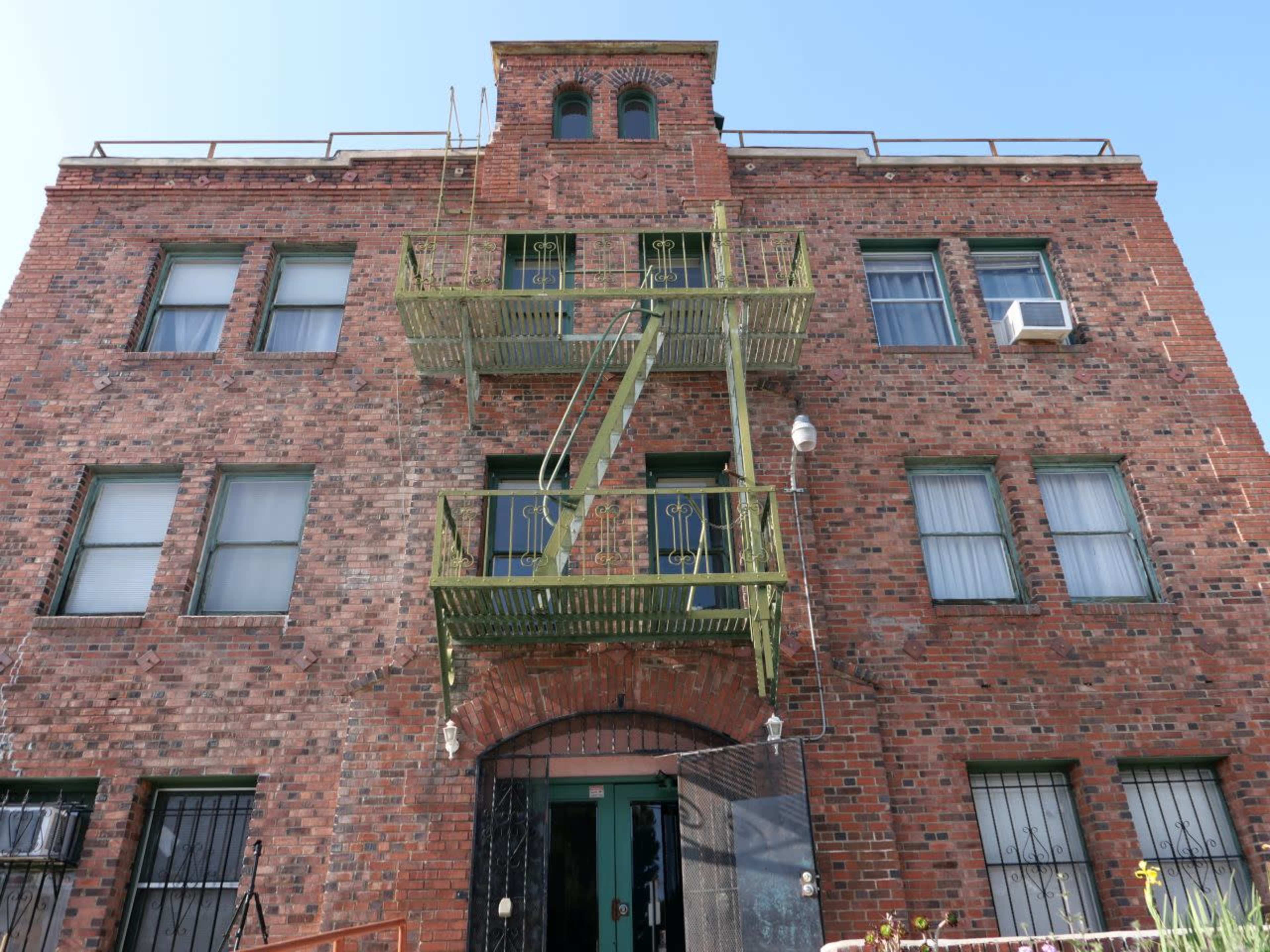 The image shows a three-story brick building with green fire escapes and multiple windows.
