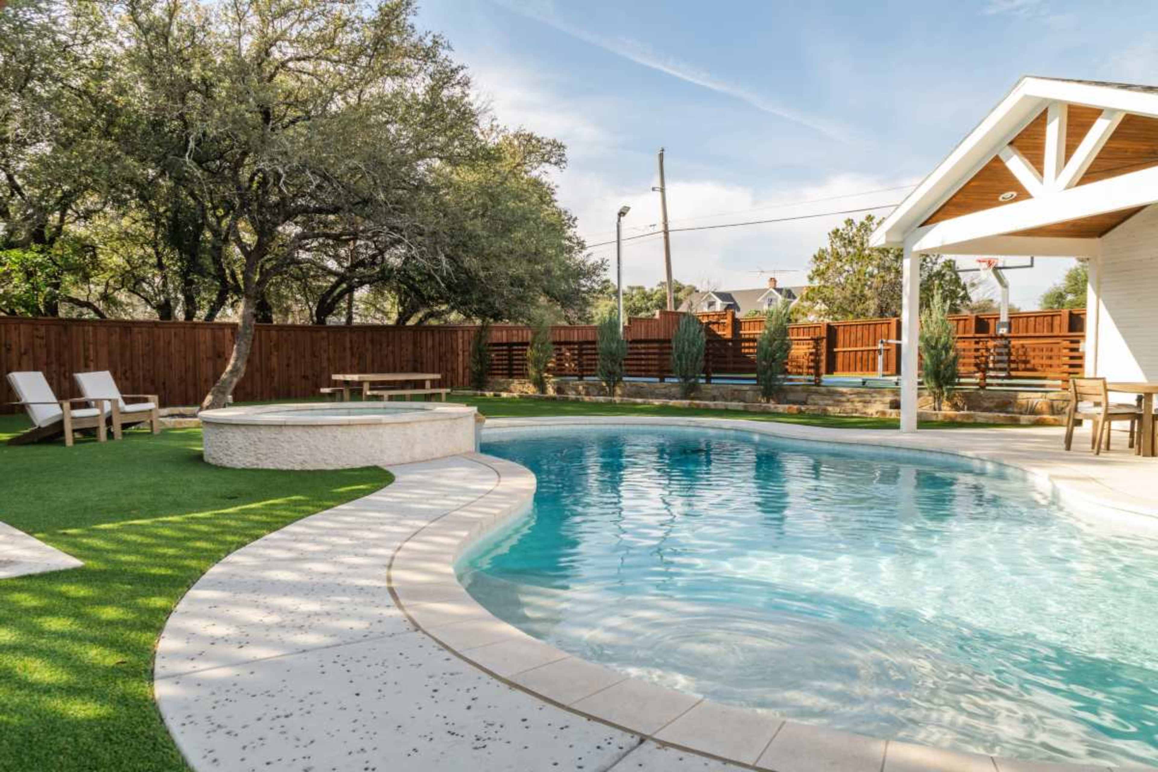 The image shows a backyard pool area featuring a rectangular pool, a spa, artificial grass, and wooden fencing.
