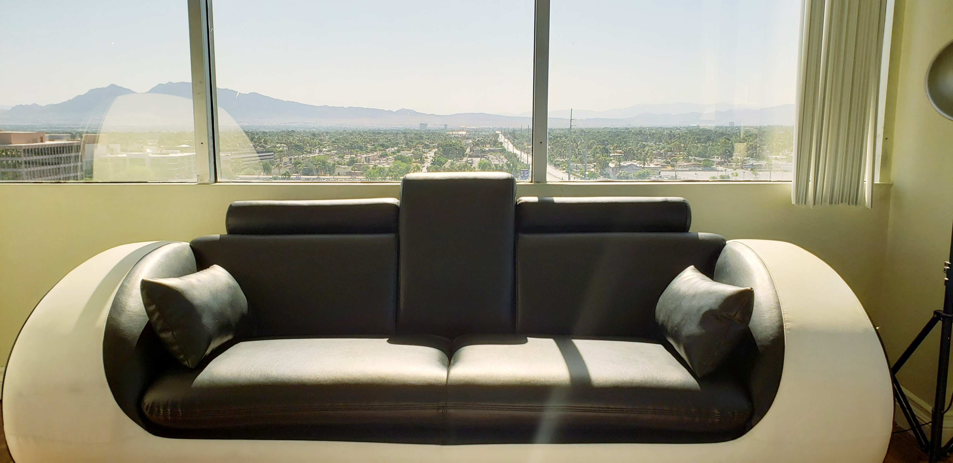 A modern black and white sofa is positioned in front of large windows, overlooking a cityscape with mountains in the background.