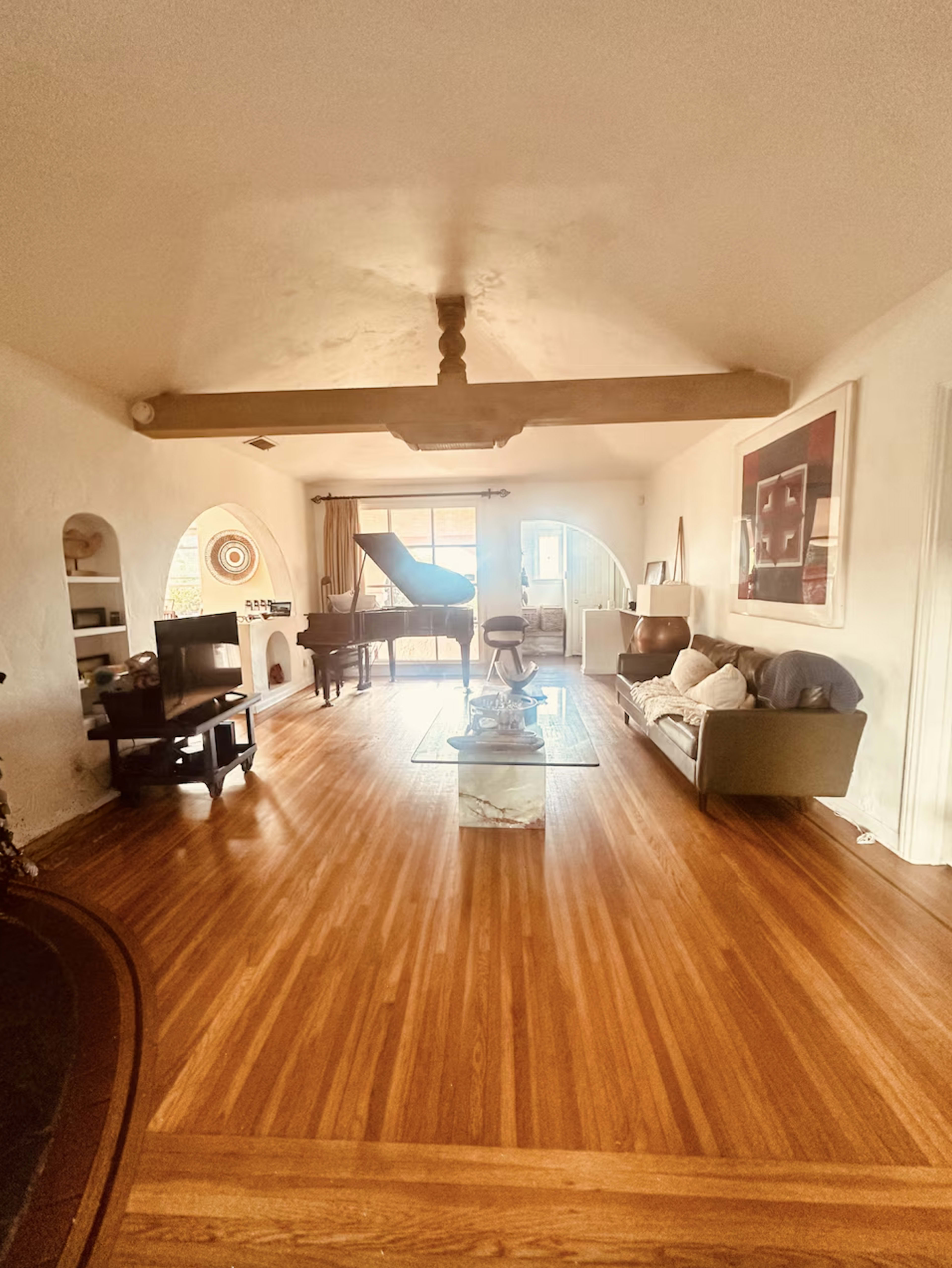 The image shows a spacious living room with hardwood floors, a grand piano, and a comfortable seating area.