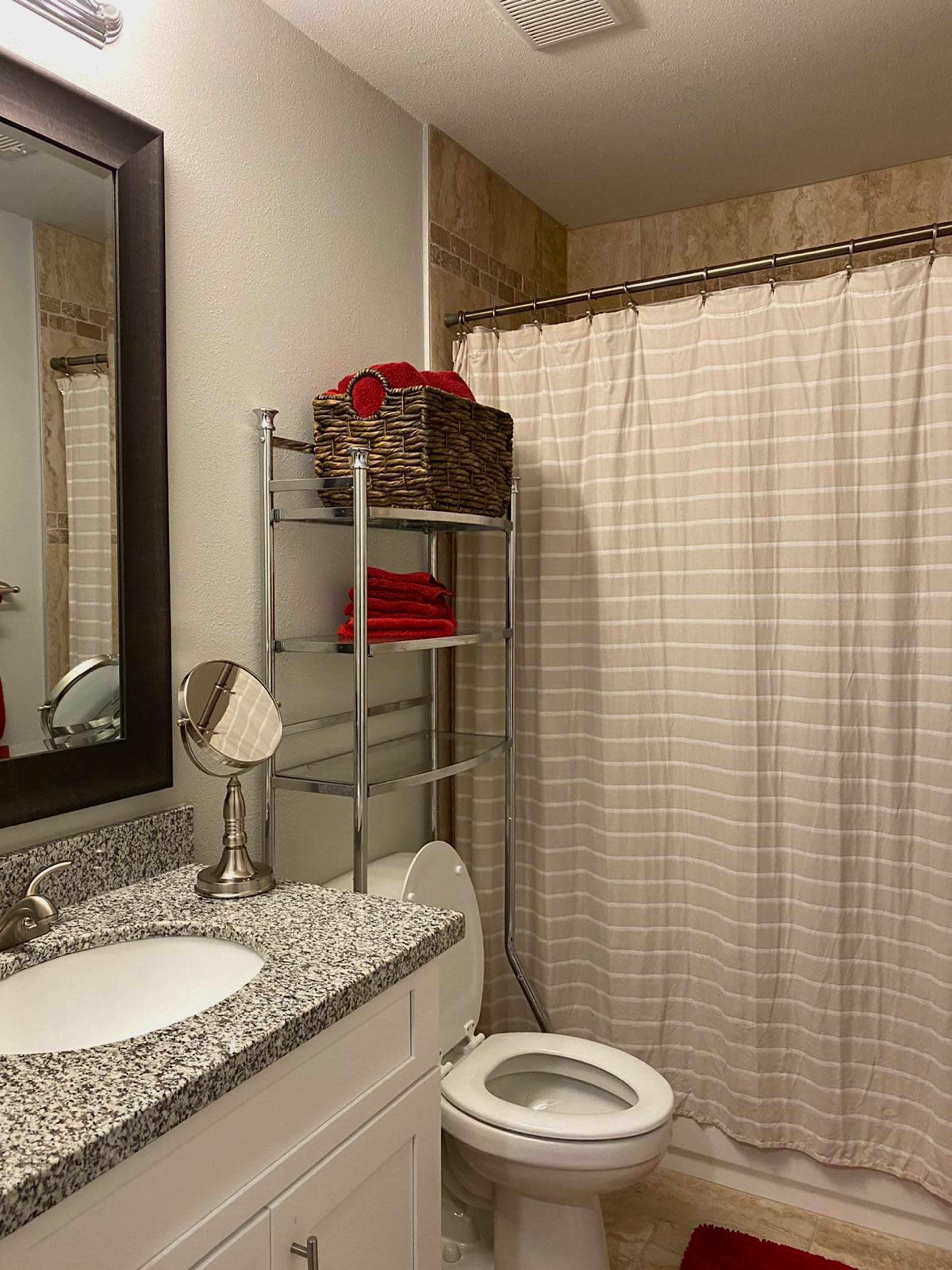 A bathroom with a sink, a mirror, a shower curtain, and shelves holding red towels.
