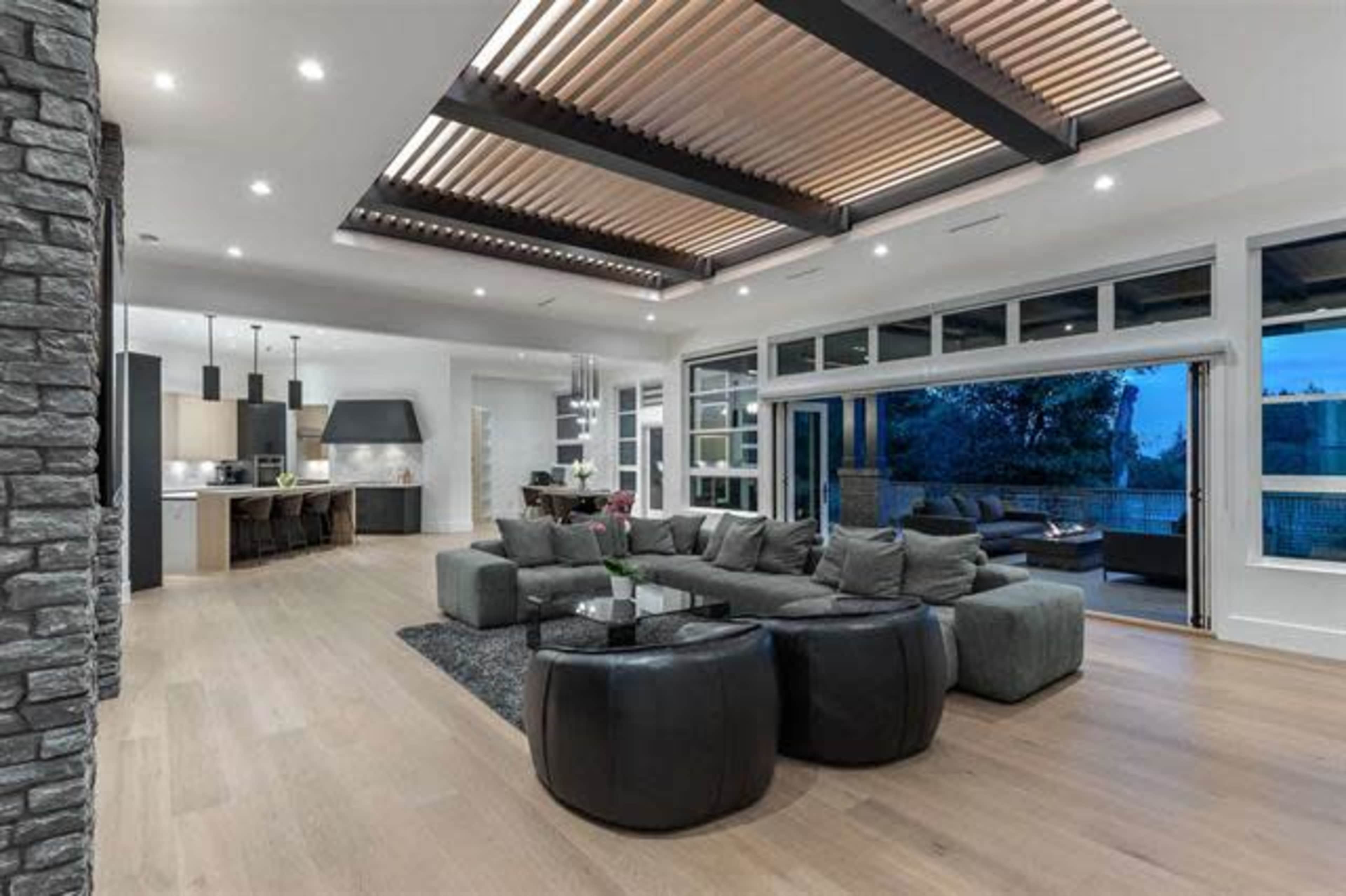 A modern living room with a large sectional sofa, stone wall accents, and expansive windows allowing for natural light.