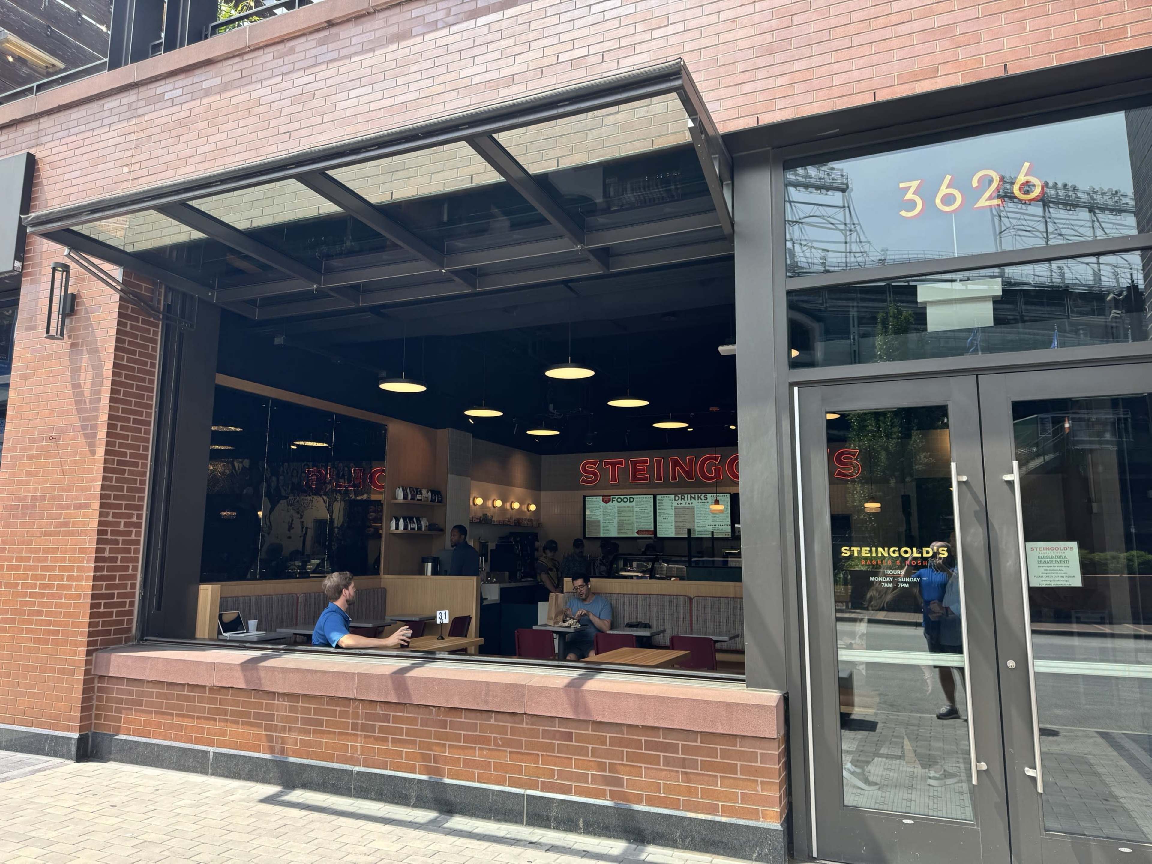The image shows a restaurant named Steingold's with large windows, where some customers are seated inside and a few are sitting at tables outside.