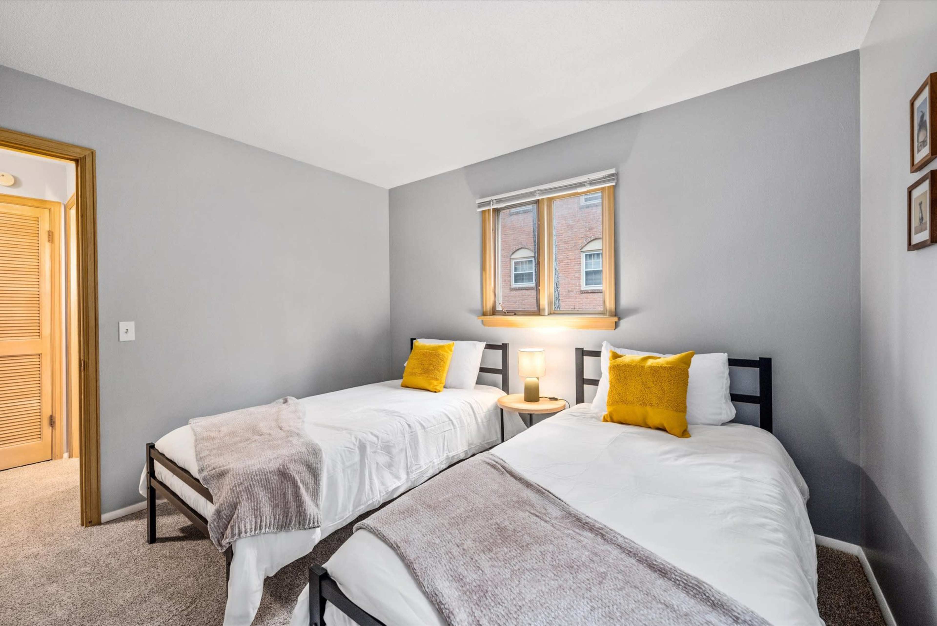 A bedroom with two single beds, a bedside table with a lamp, and a window that brings in natural light.