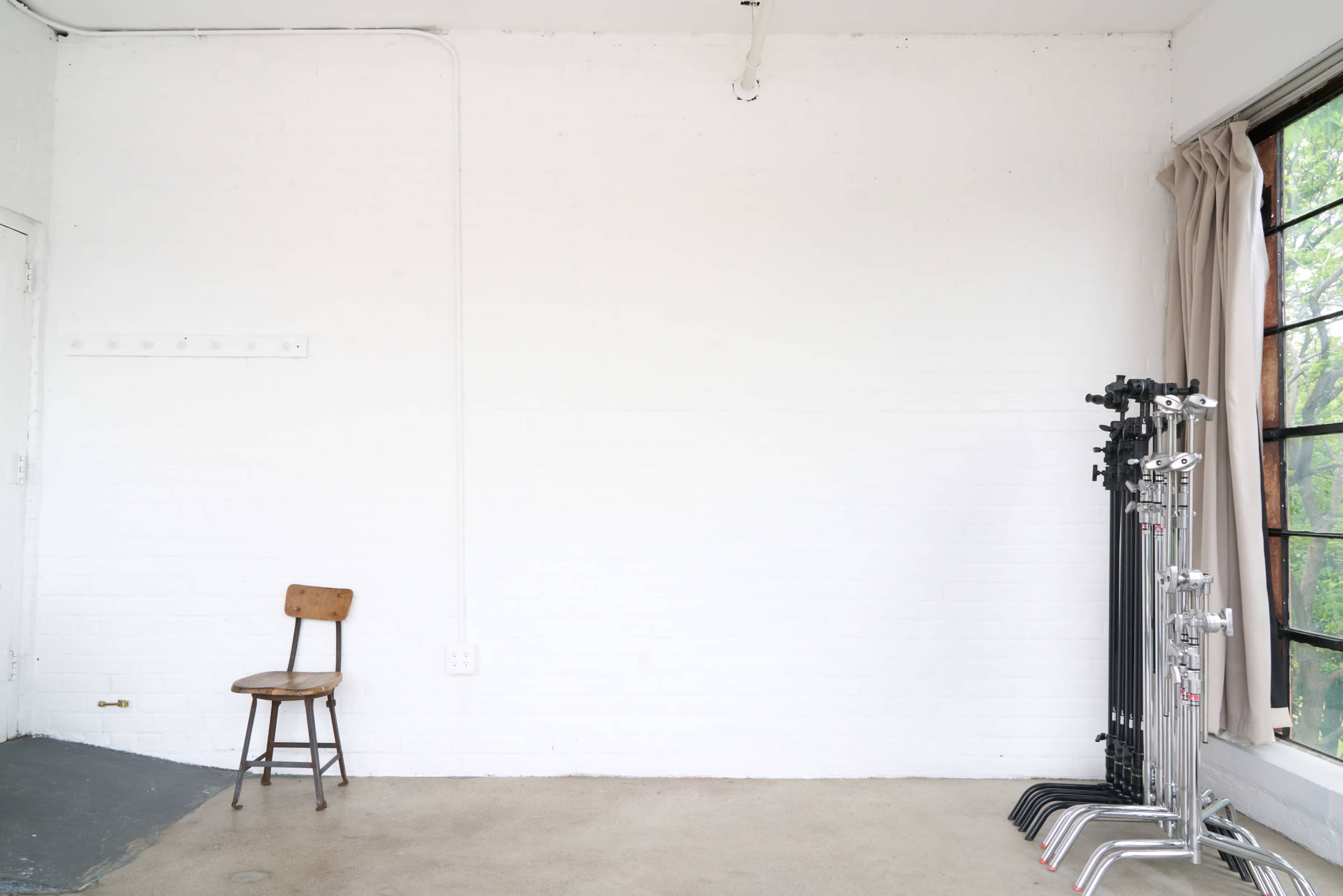 The image shows an empty room with a wooden chair against a white brick wall and several light stands positioned in the corner.