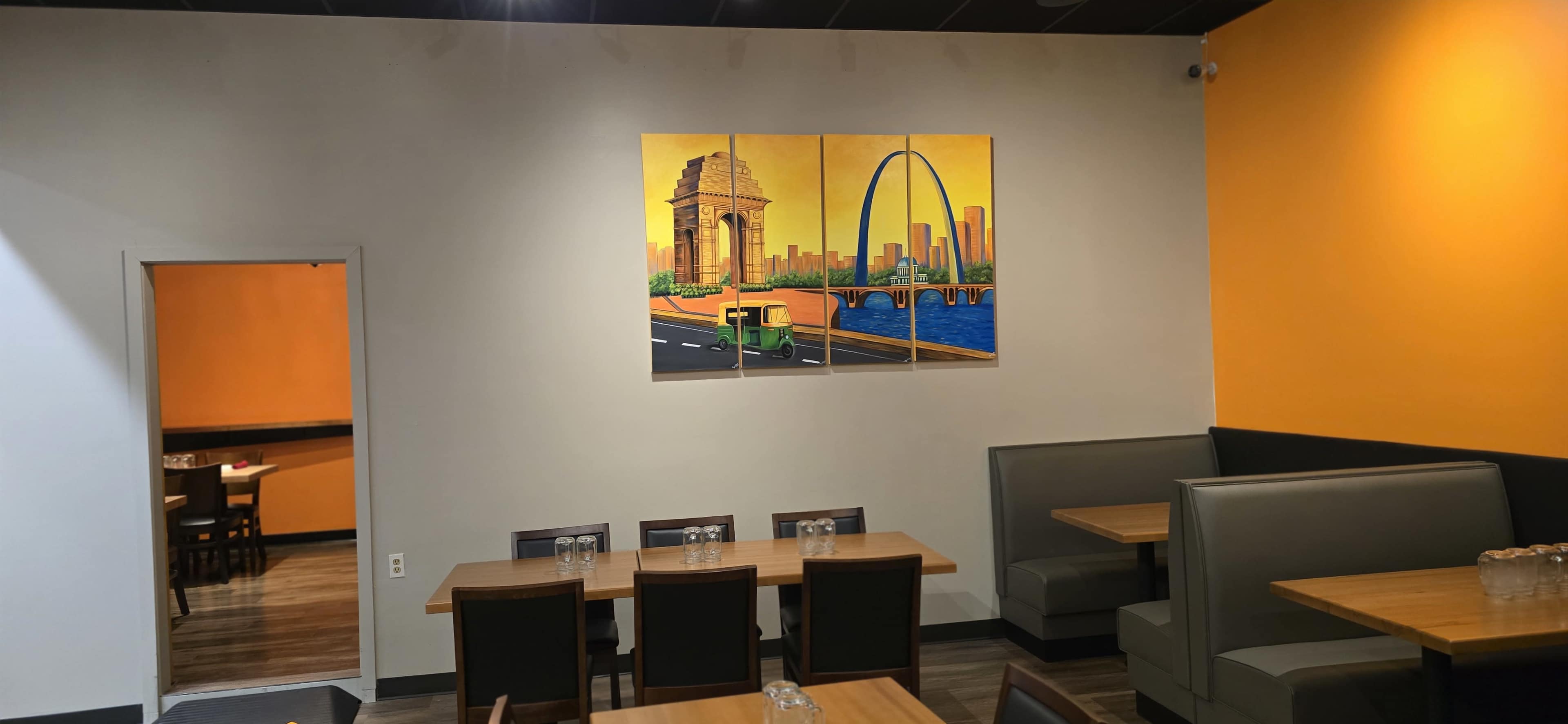 The interior of a restaurant features a vibrant orange wall with an artwork depicting a city skyline and a bridge.