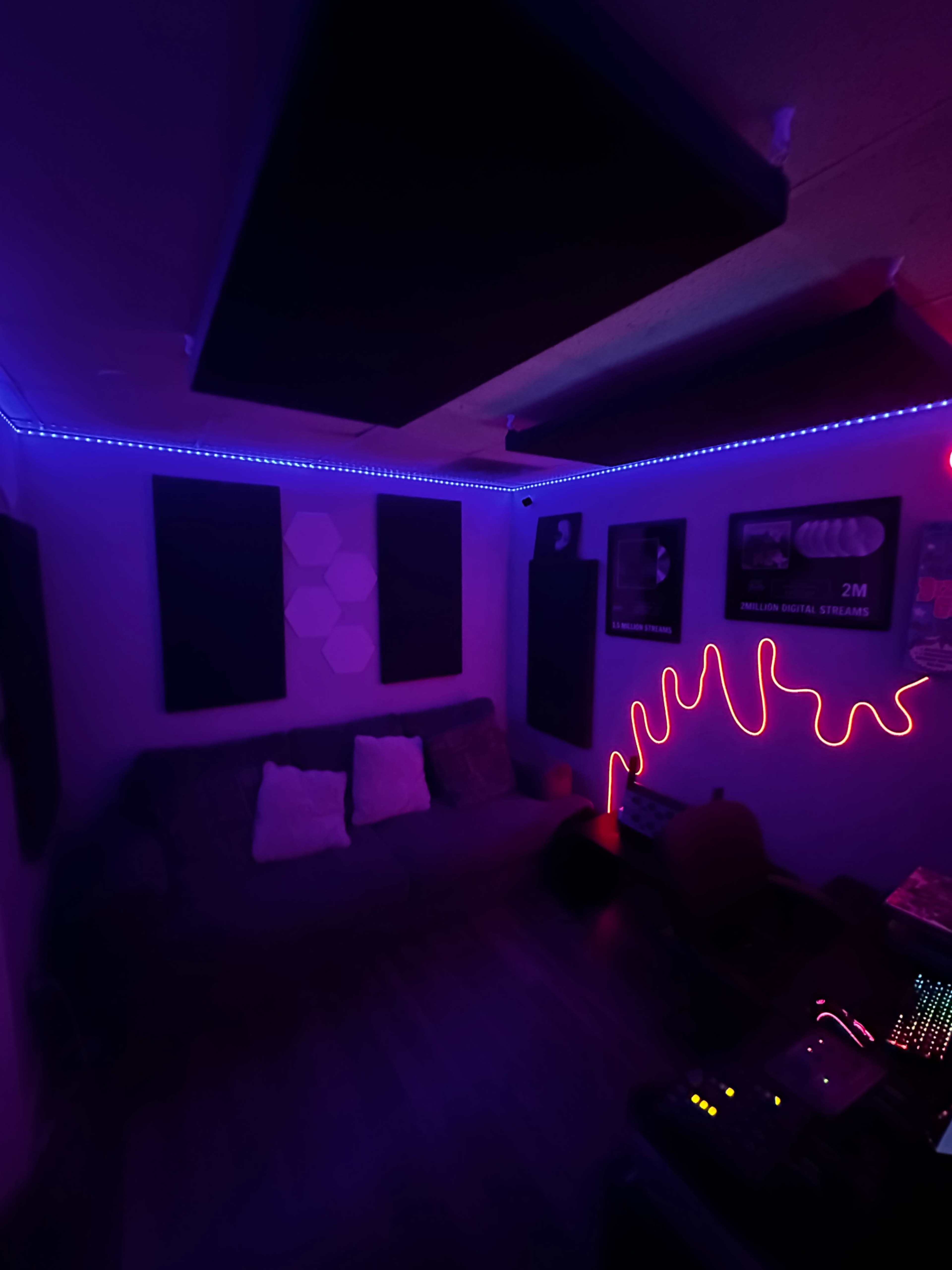 The image shows a dimly lit music studio with purple and blue lights, a couch, sound panels on the walls, and a glowing neon design.