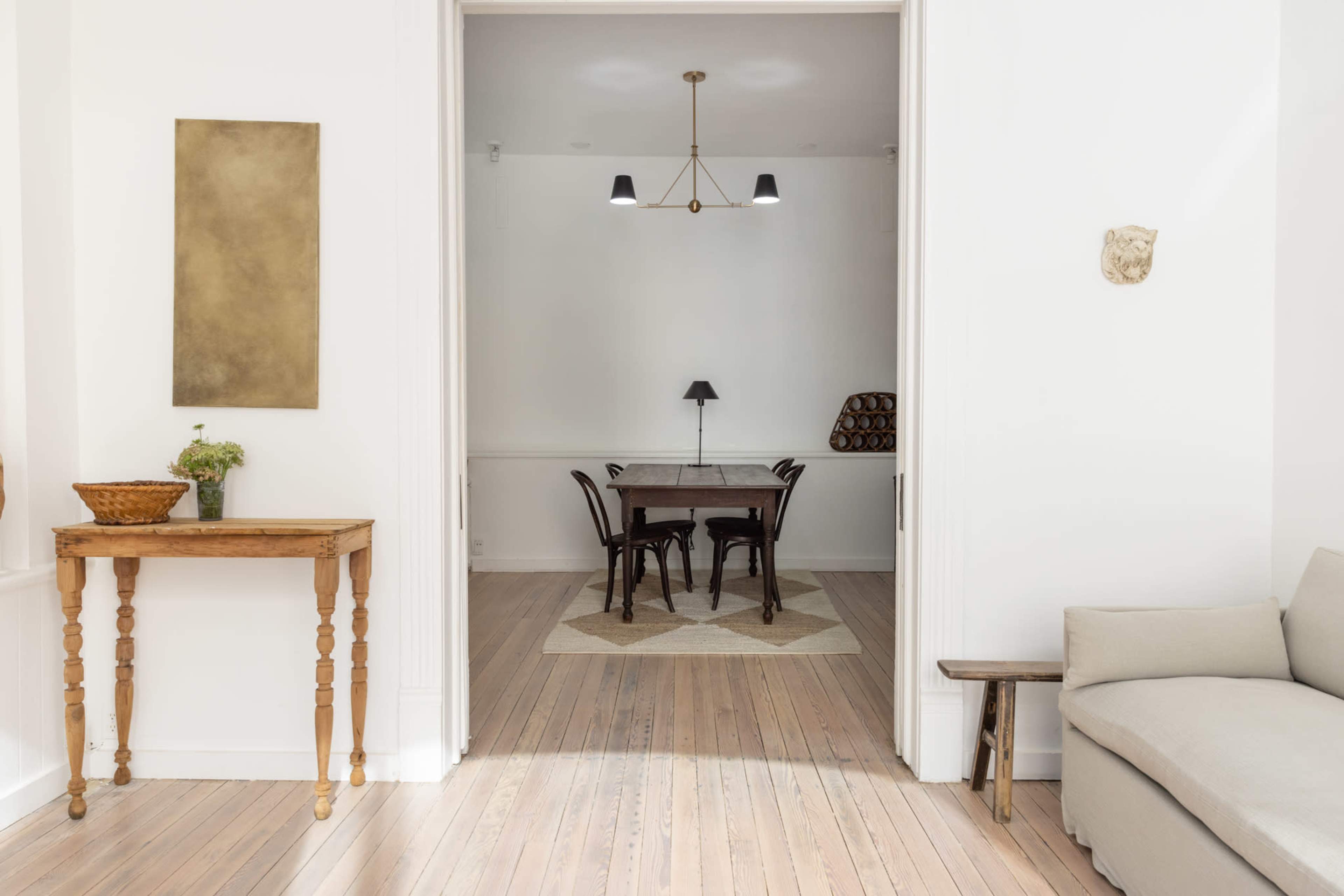 A light-filled interior shows a wooden table surrounded by chairs, visible through an open doorway.