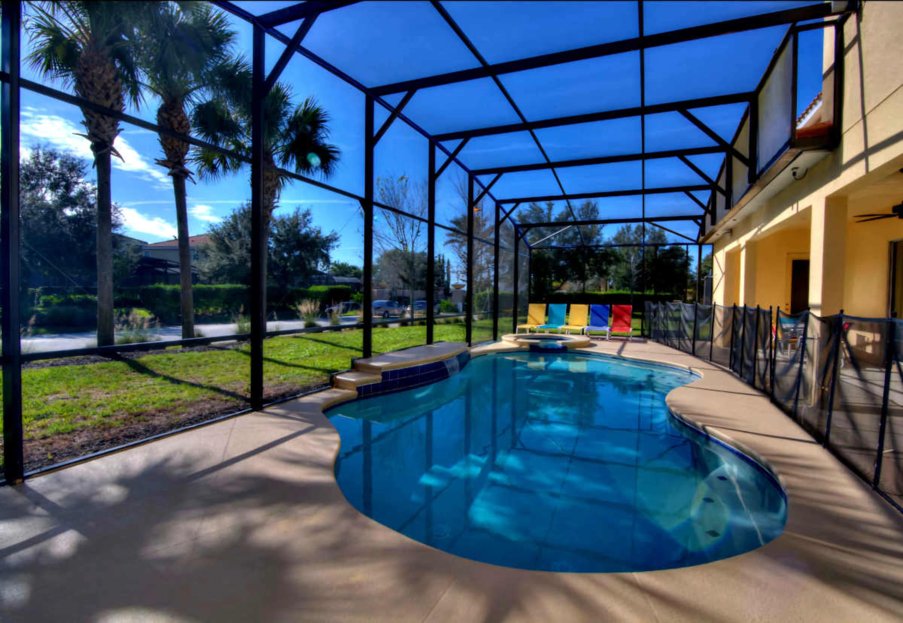 The image shows a screened-in pool area with a blue pool surrounded by lounge chairs and palm trees.