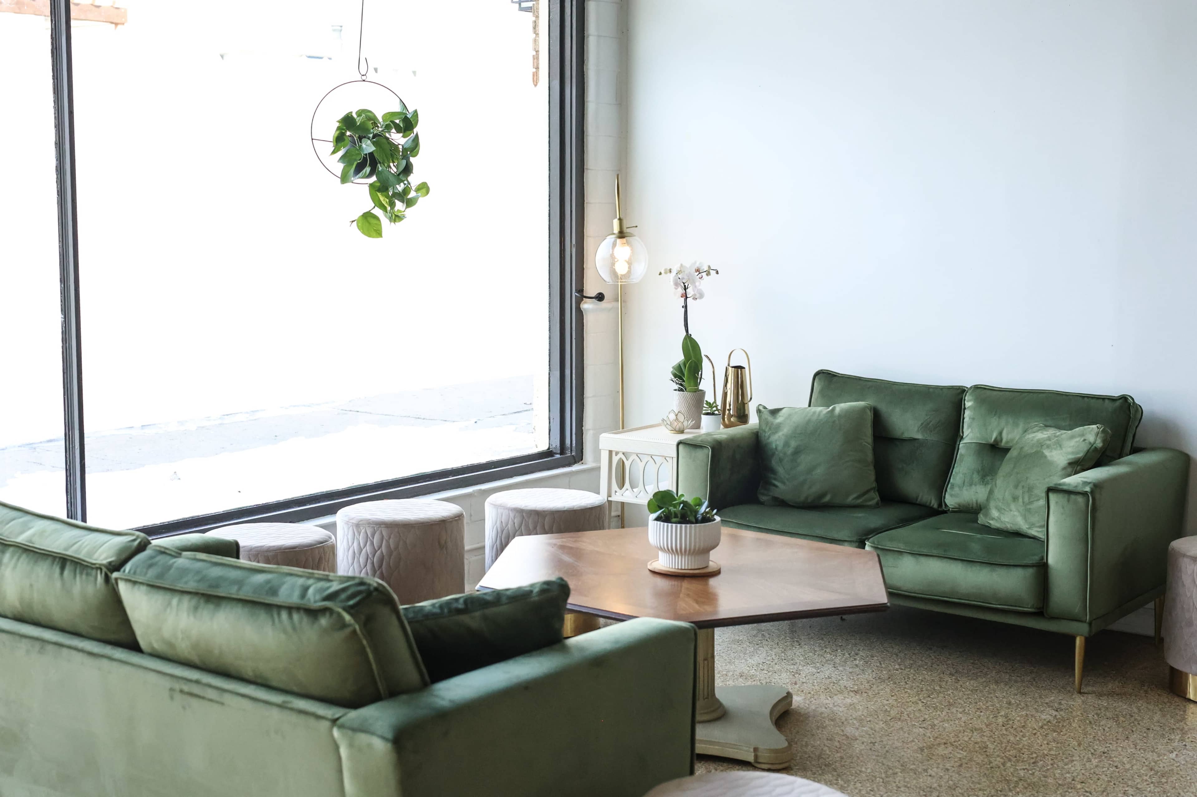 A modern lounge area features green sofas, a wooden coffee table, and large windows with natural light.