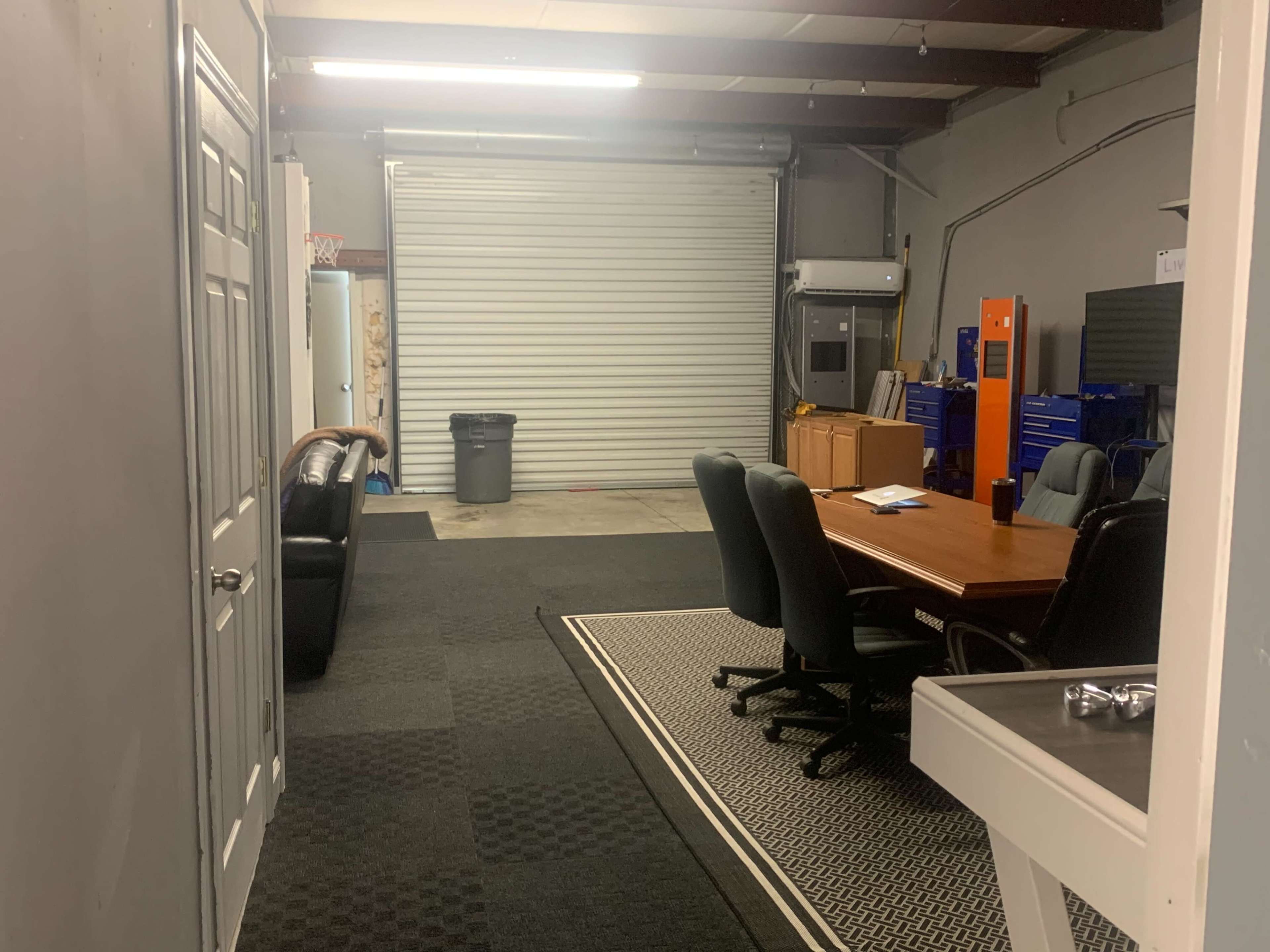 A spacious office area with a wooden conference table surrounded by black chairs, a couch, and a large roll-up door at the back.
