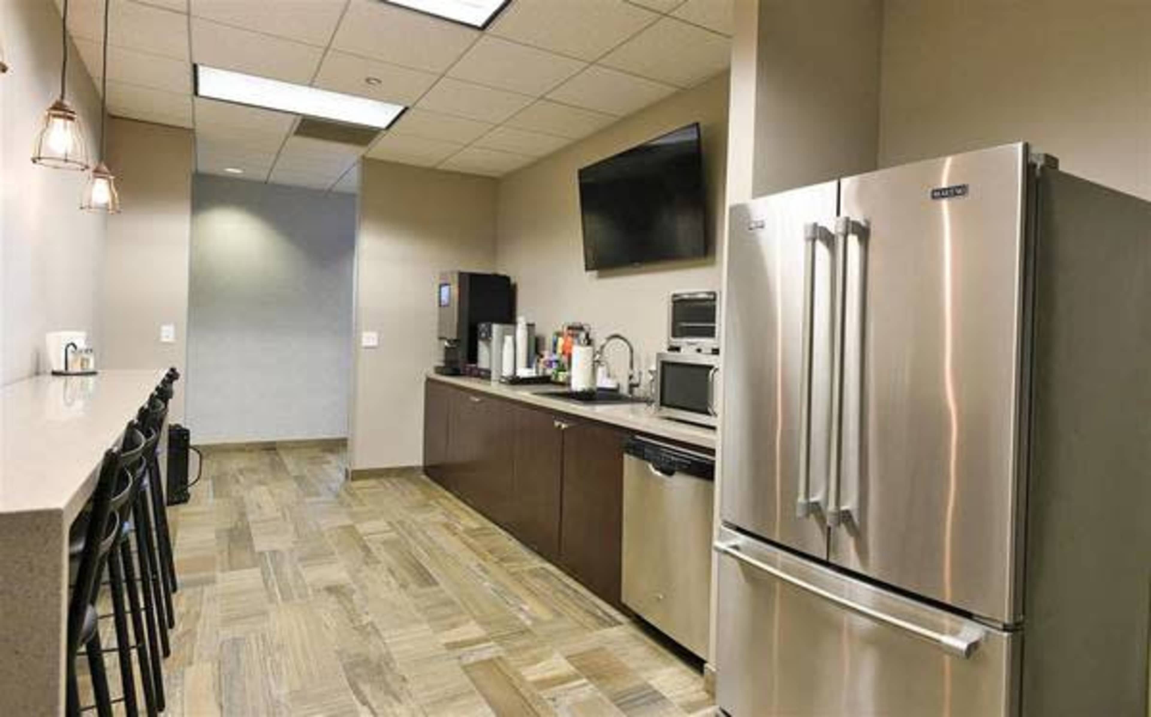 The image shows a modern kitchen area with stainless steel appliances, a countertop, and seating along one side.