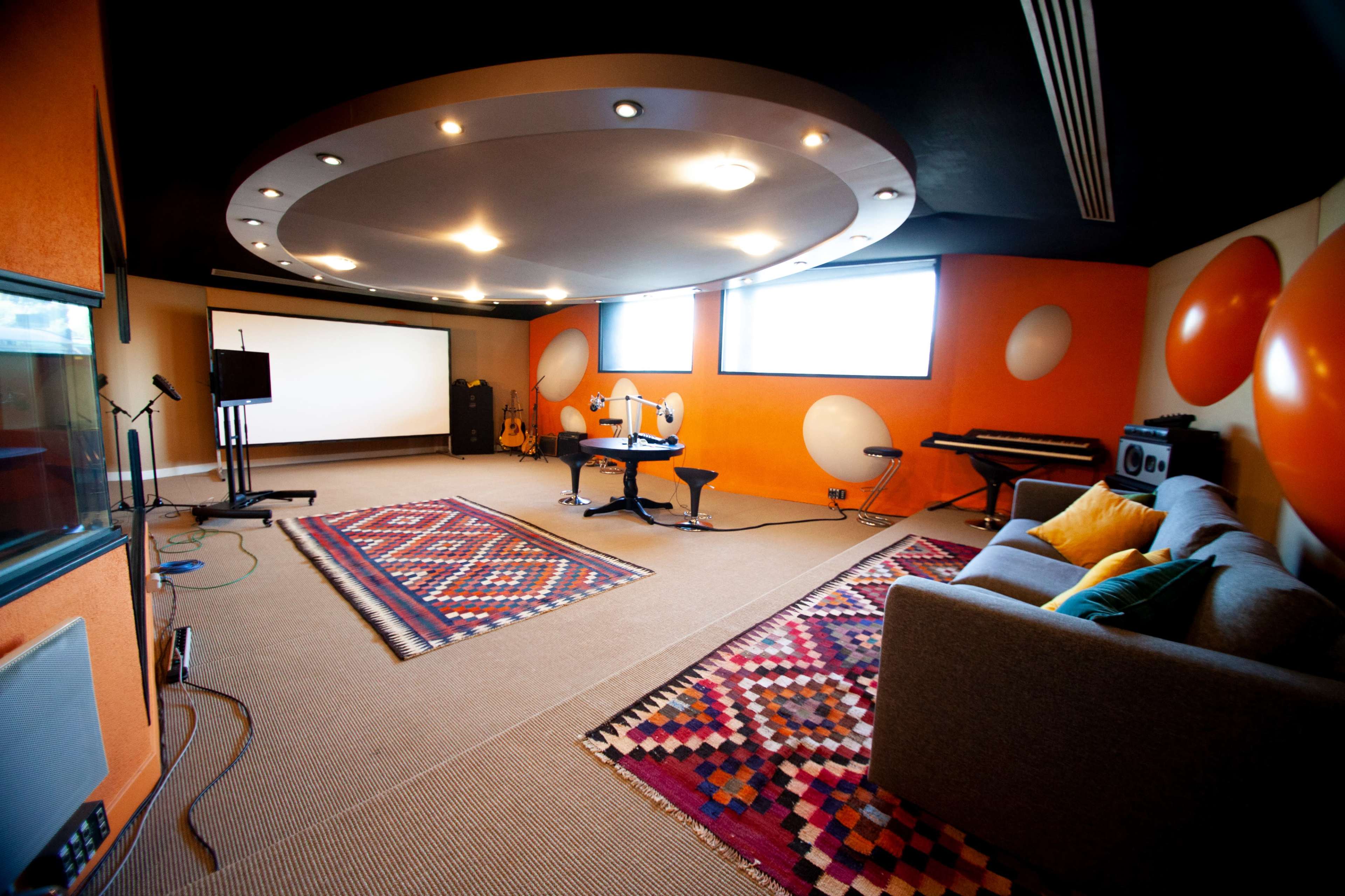 A modern recording studio featuring a large central rug, seating area, audio equipment, and colorful wall decor.