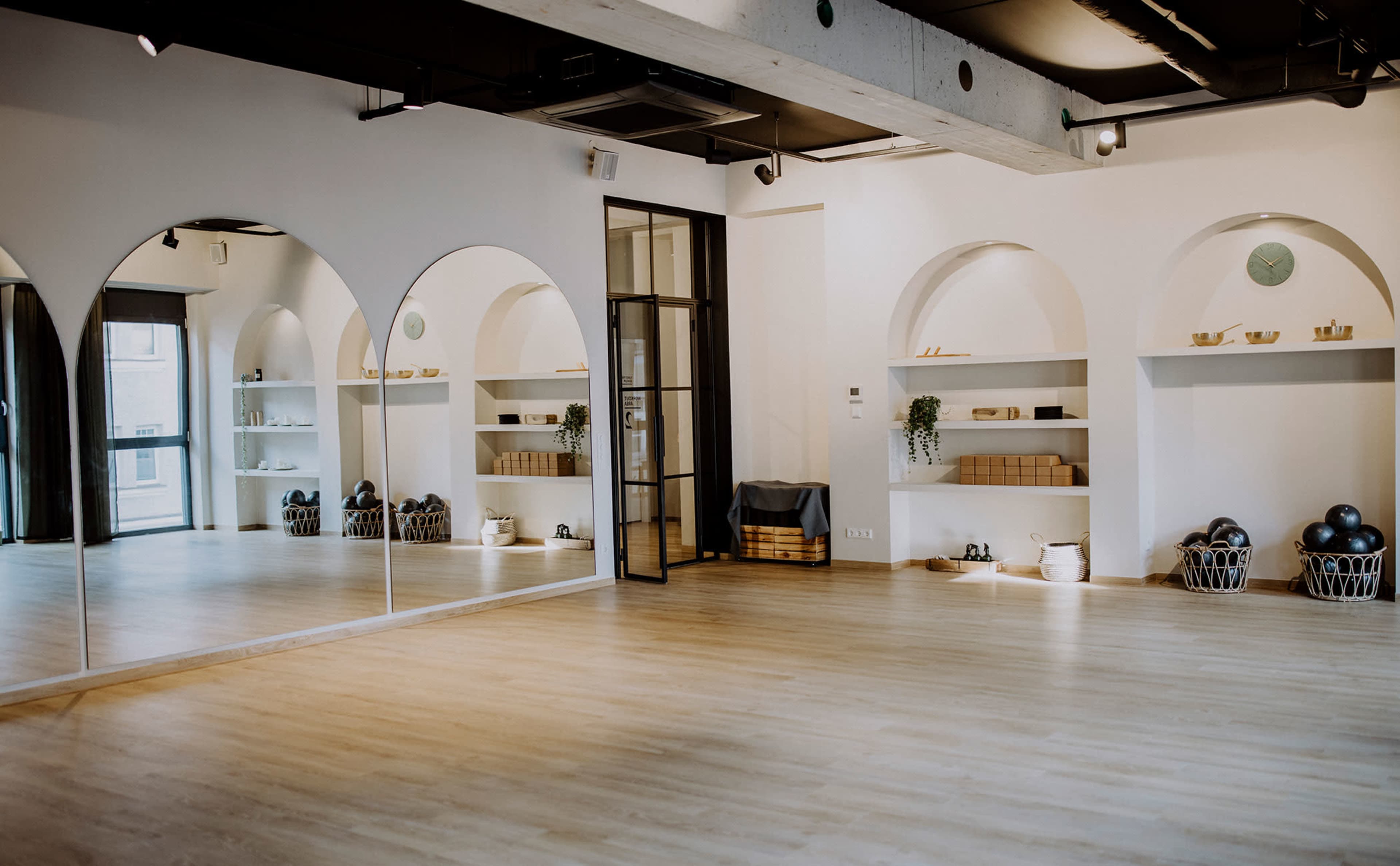 The image shows a spacious, well-lit studio with arched wall niches displaying neatly arranged fitness equipment and decor.