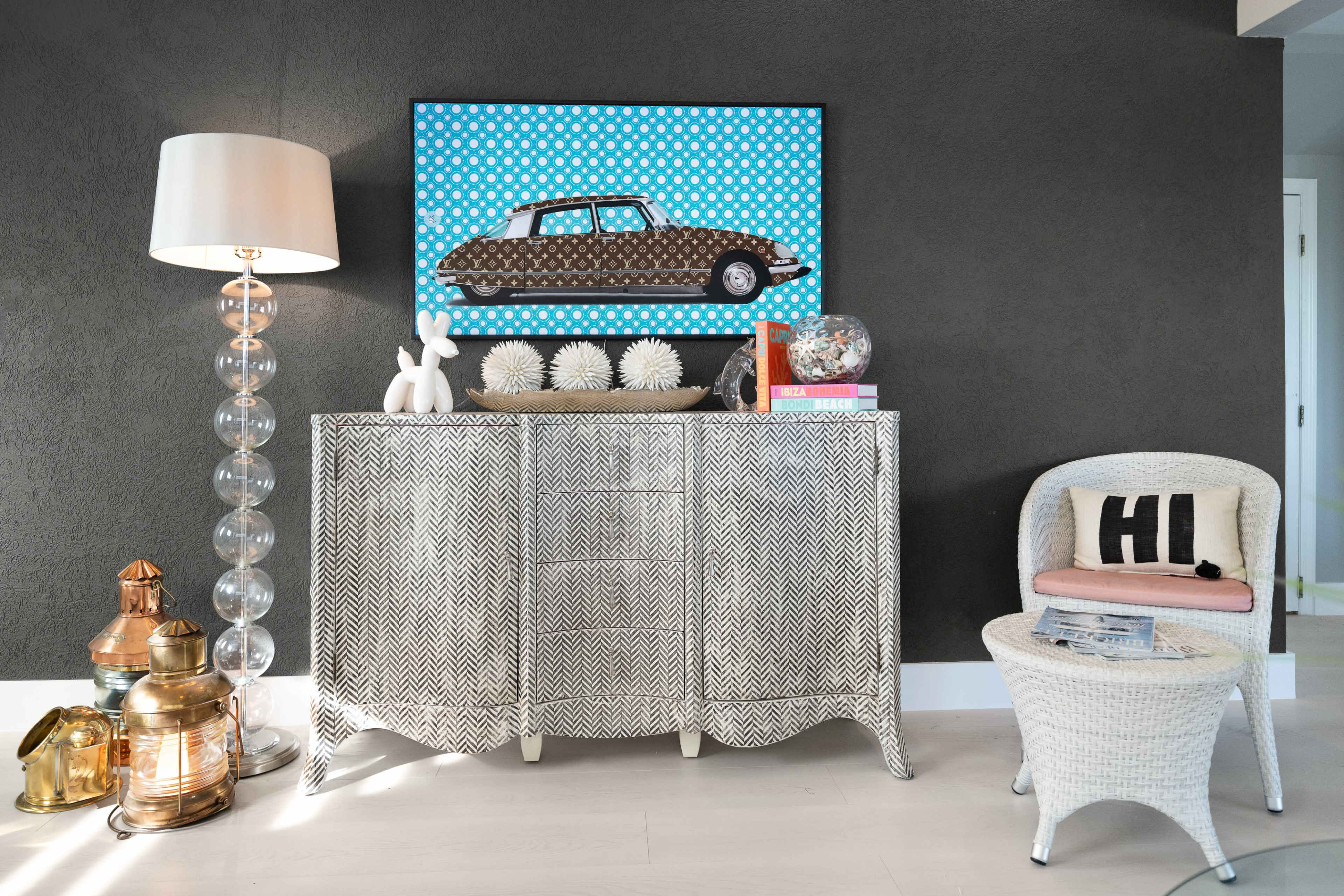 A stylish corner features a patterned sideboard, a decorative lamp, and a framed artwork of a car against a polka-dotted background.