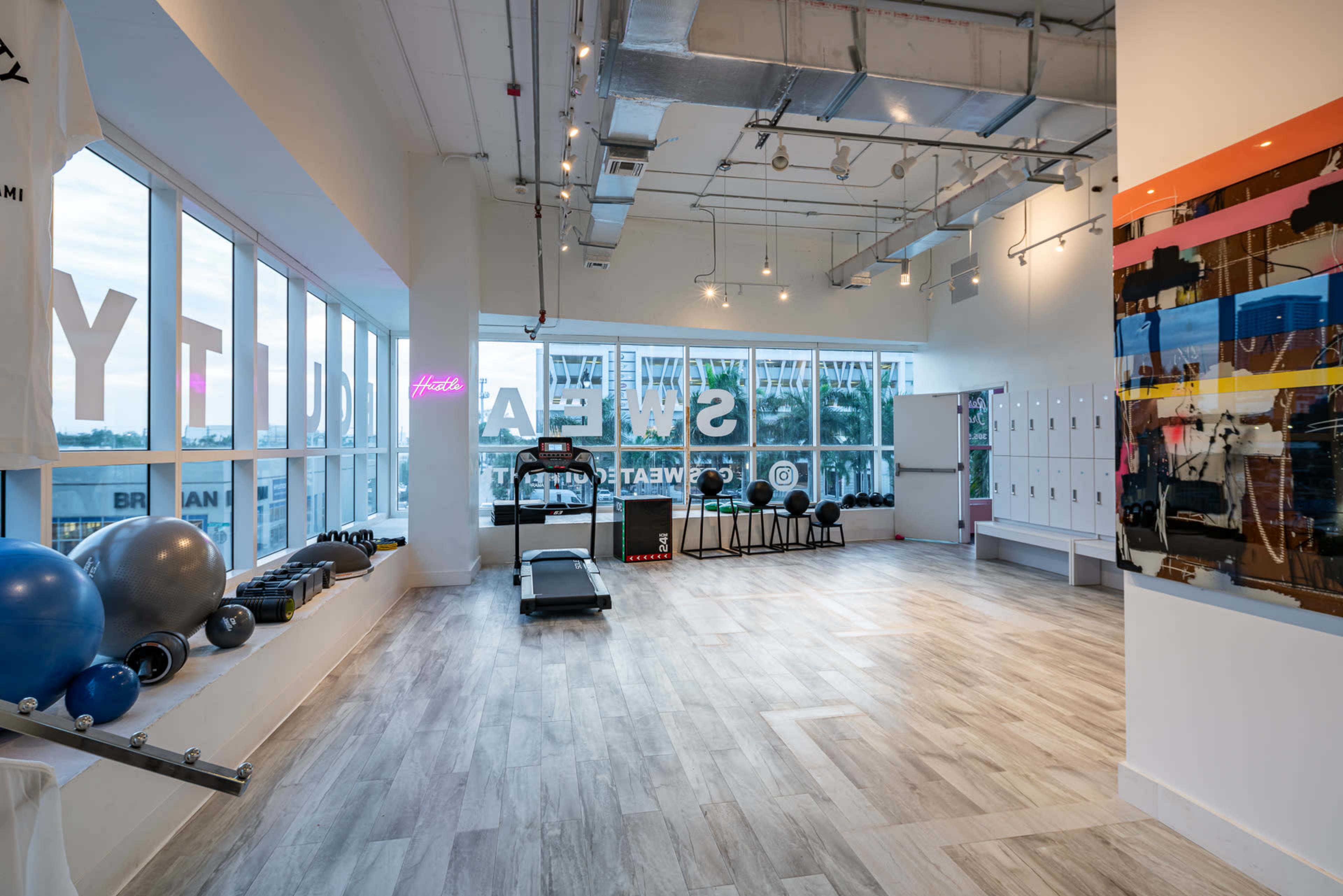The image shows a modern gym interior with exercise equipment, large windows, and a vibrant color scheme.