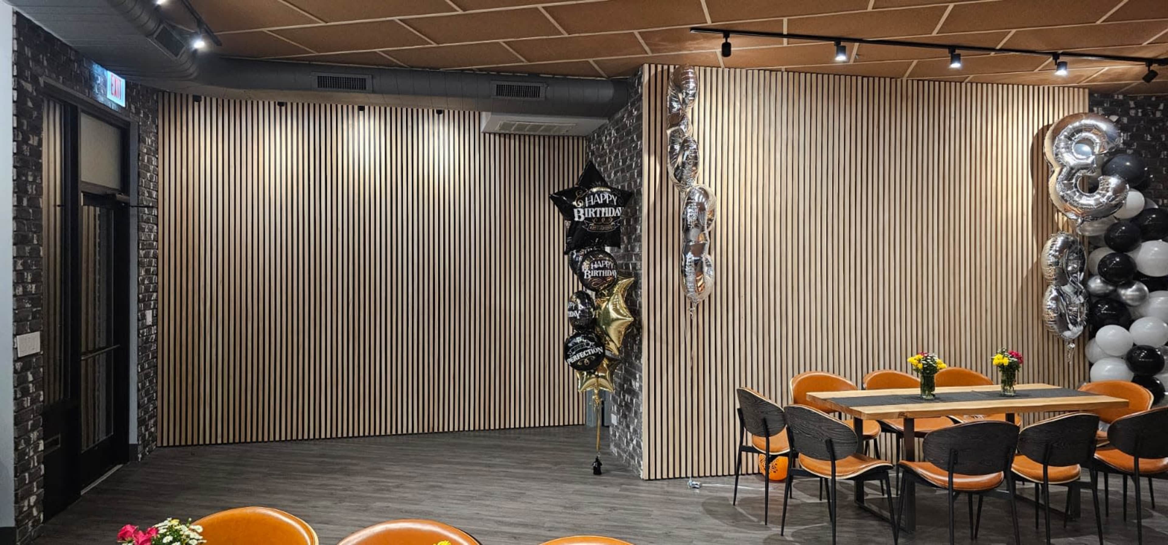 A contemporary interior design featuring a wooden slatted wall, a table set for dining, and decorations including balloons on one side.