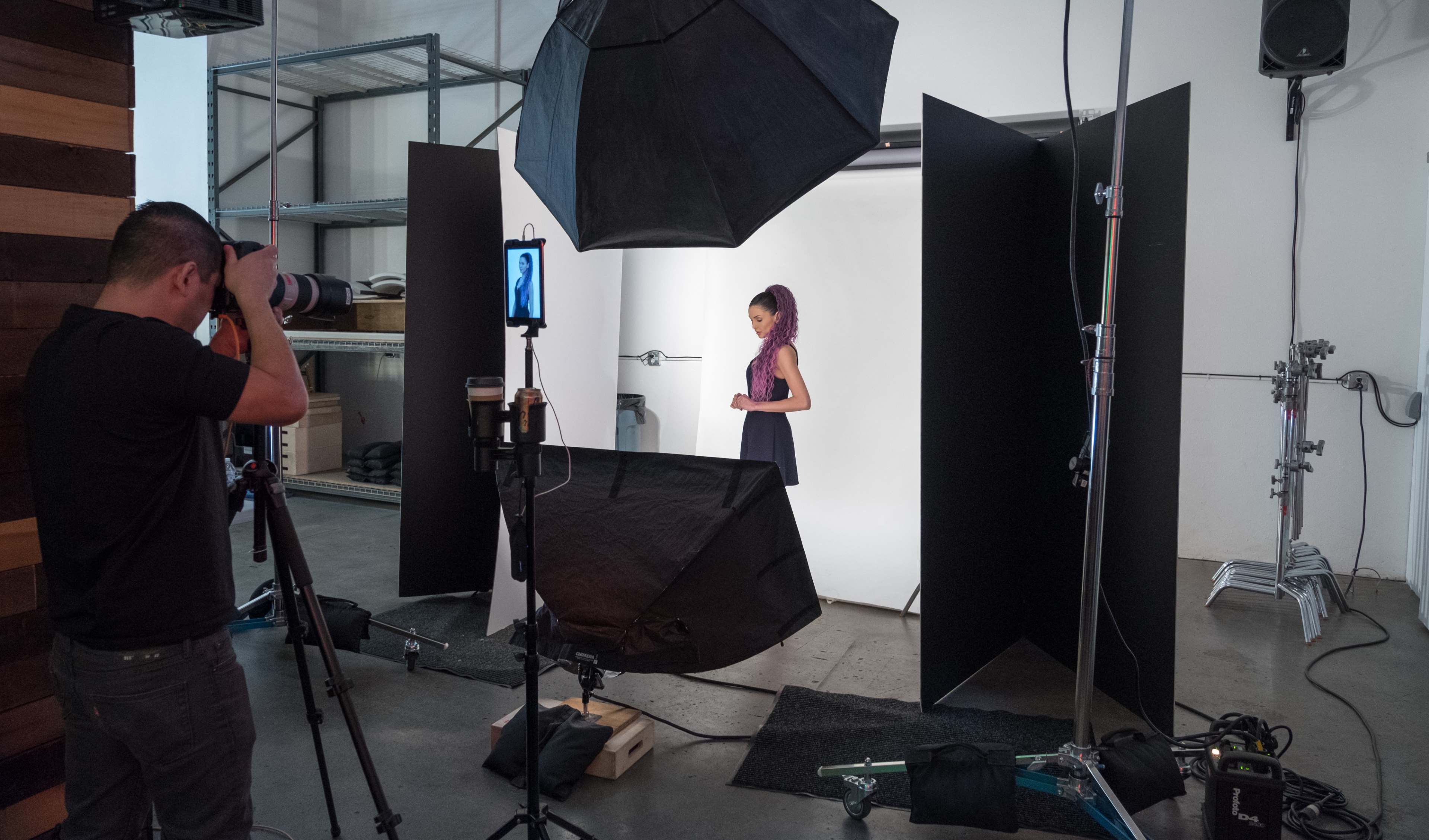 A photographer is capturing images of a girl standing in front of a backdrop in a studio setup with various lighting equipment.