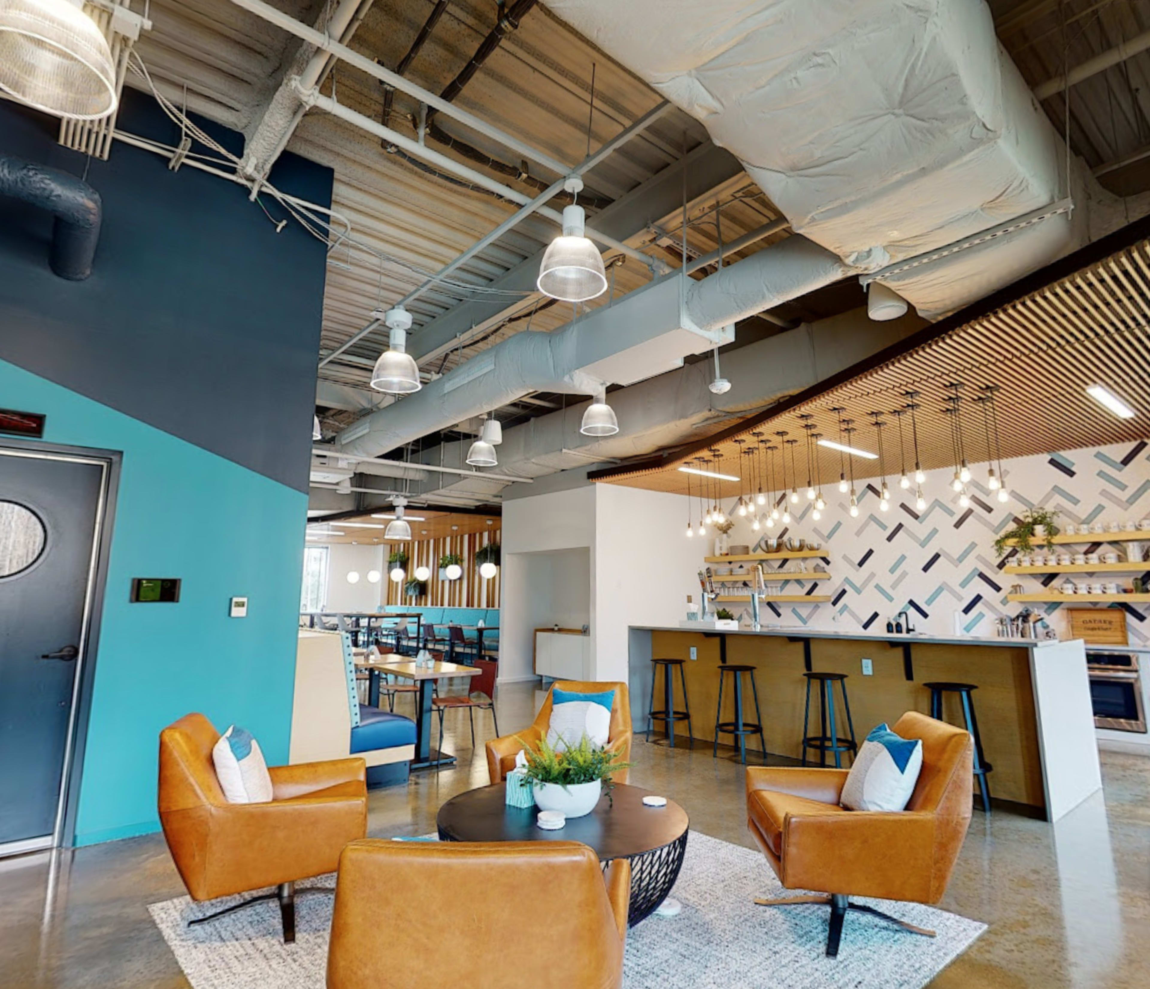 A modern lounge area with brown leather chairs around a circular table and a bar with shelving in the background.