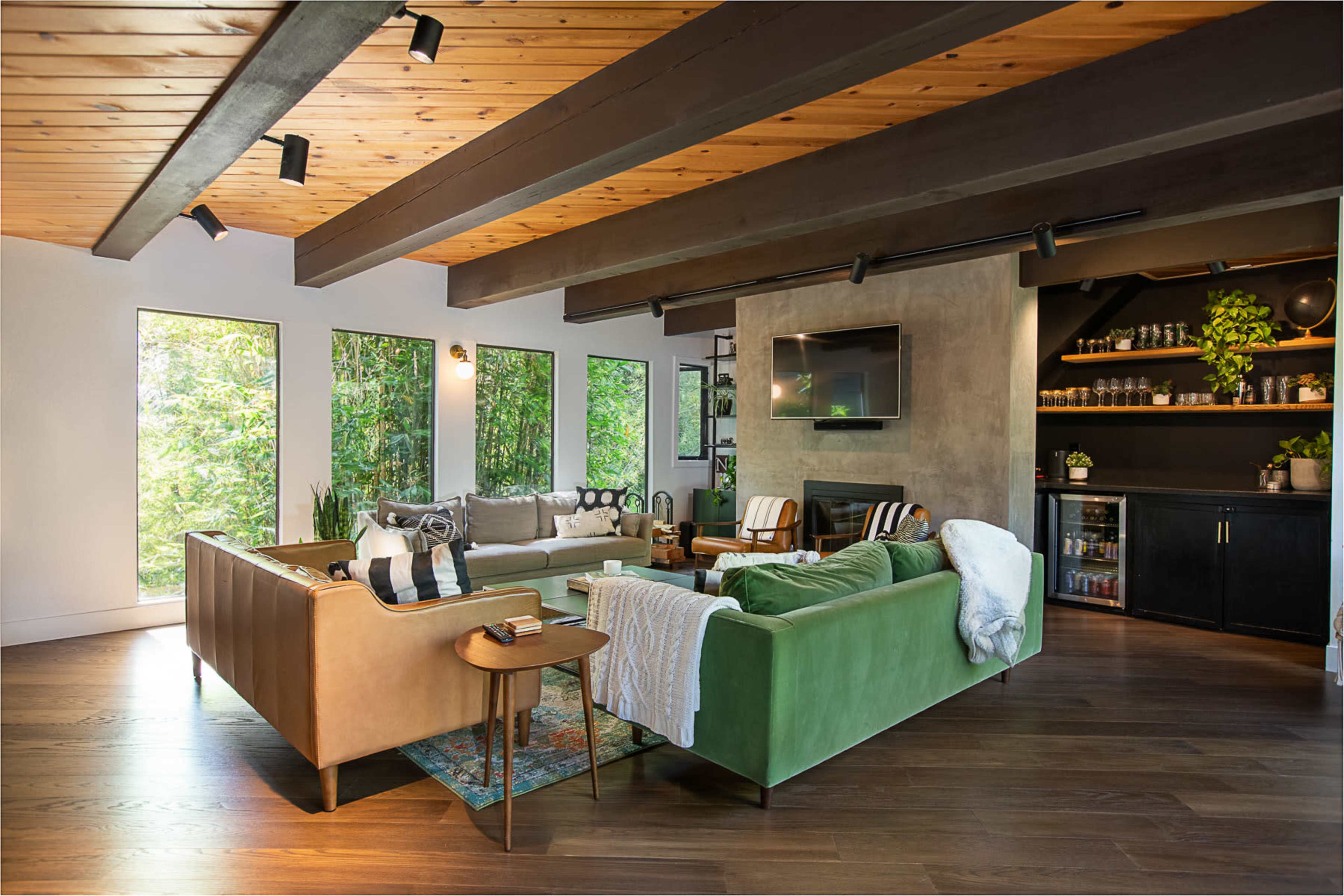 The living room features two sofas, large windows with views of greenery, and a built-in shelf displaying plants and decor.